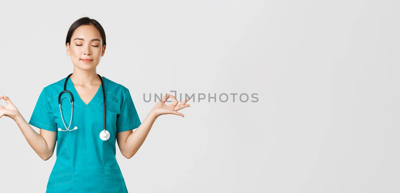 Covid-19, healthcare workers and preventing virus concept. Calm and patient asian female doctor, nurse in scrubs staying relaxed, meditating with eyes closed and happy smile, white background by Benzoix