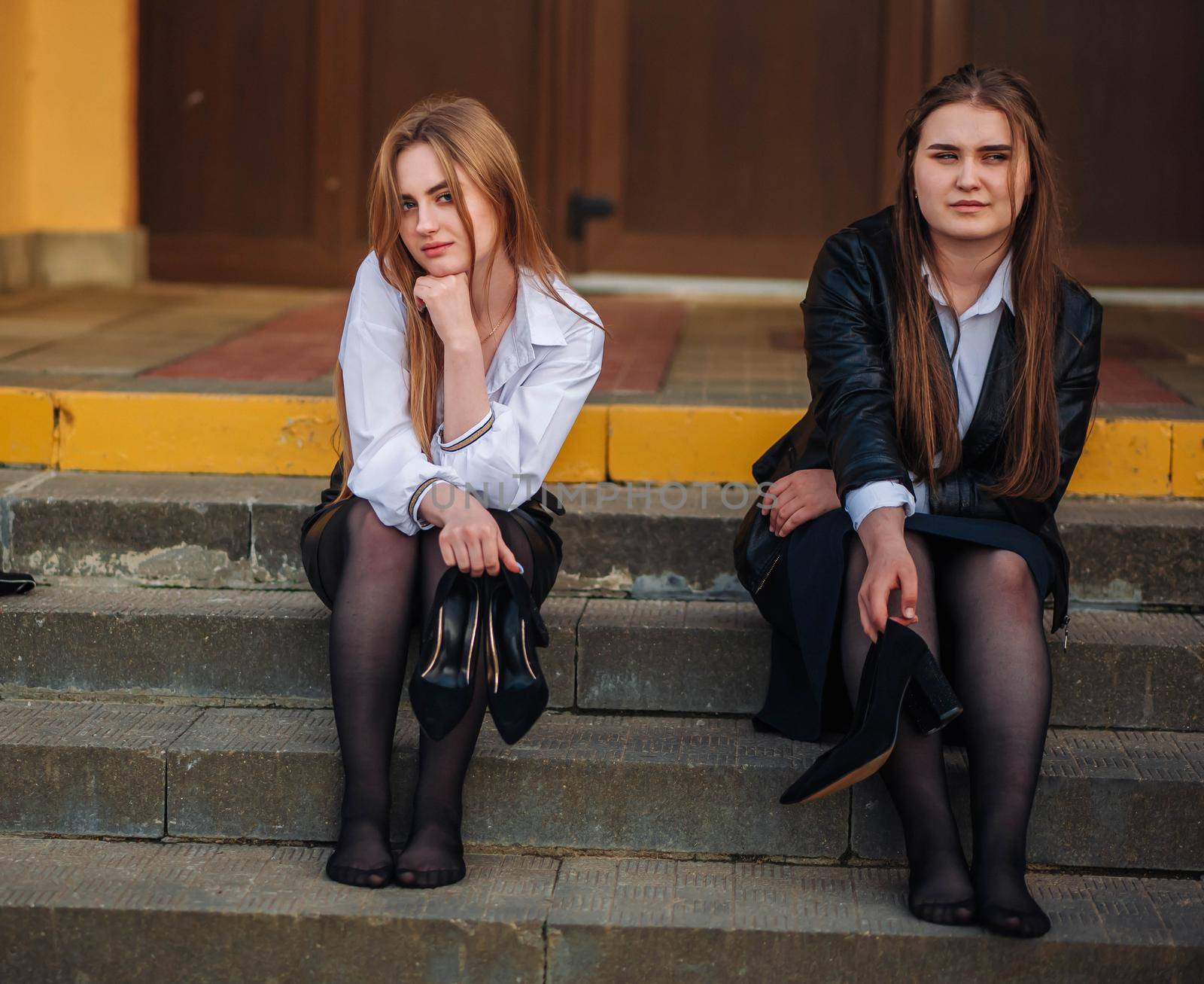 Tired schoolgirls sit barefoot on the steps of the school