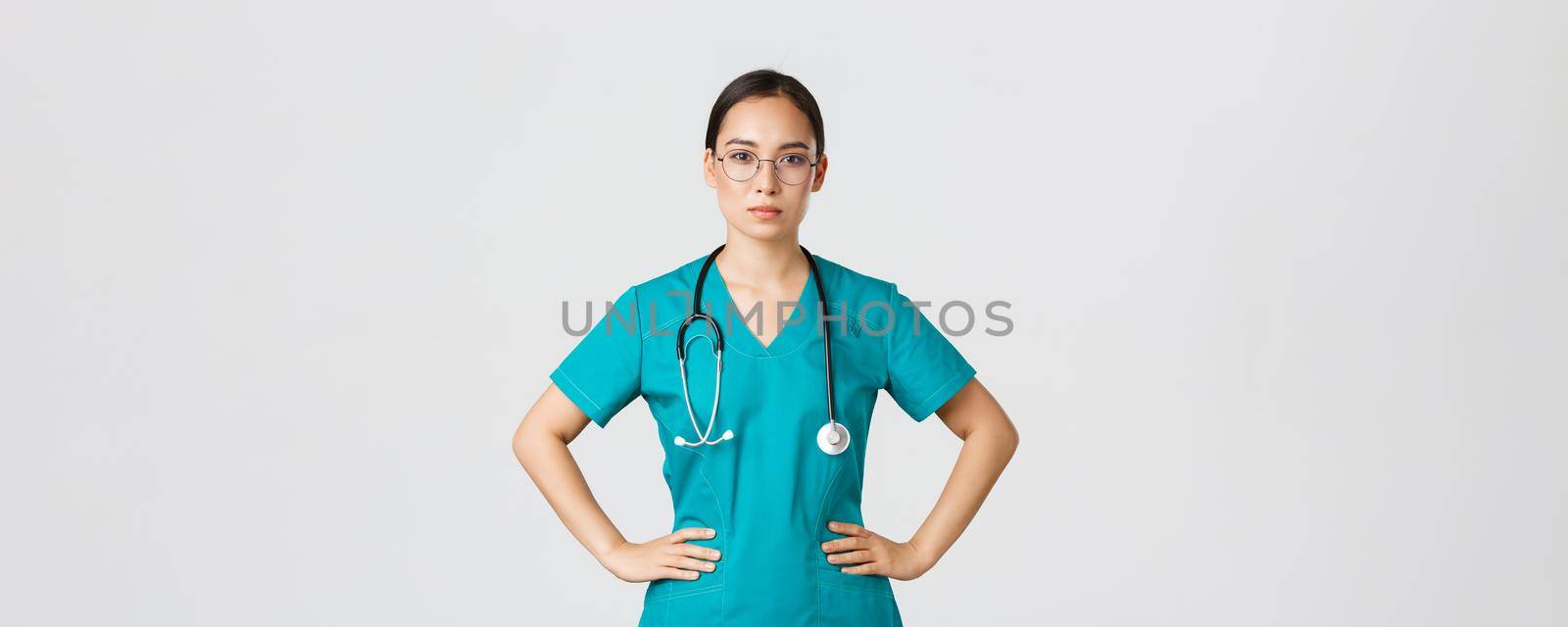 Covid-19, healthcare workers, pandemic concept. Confident determined asian female nurse helping patients, working with coronavirus disease, looking ready, wearing scrubs and glasses, white background.