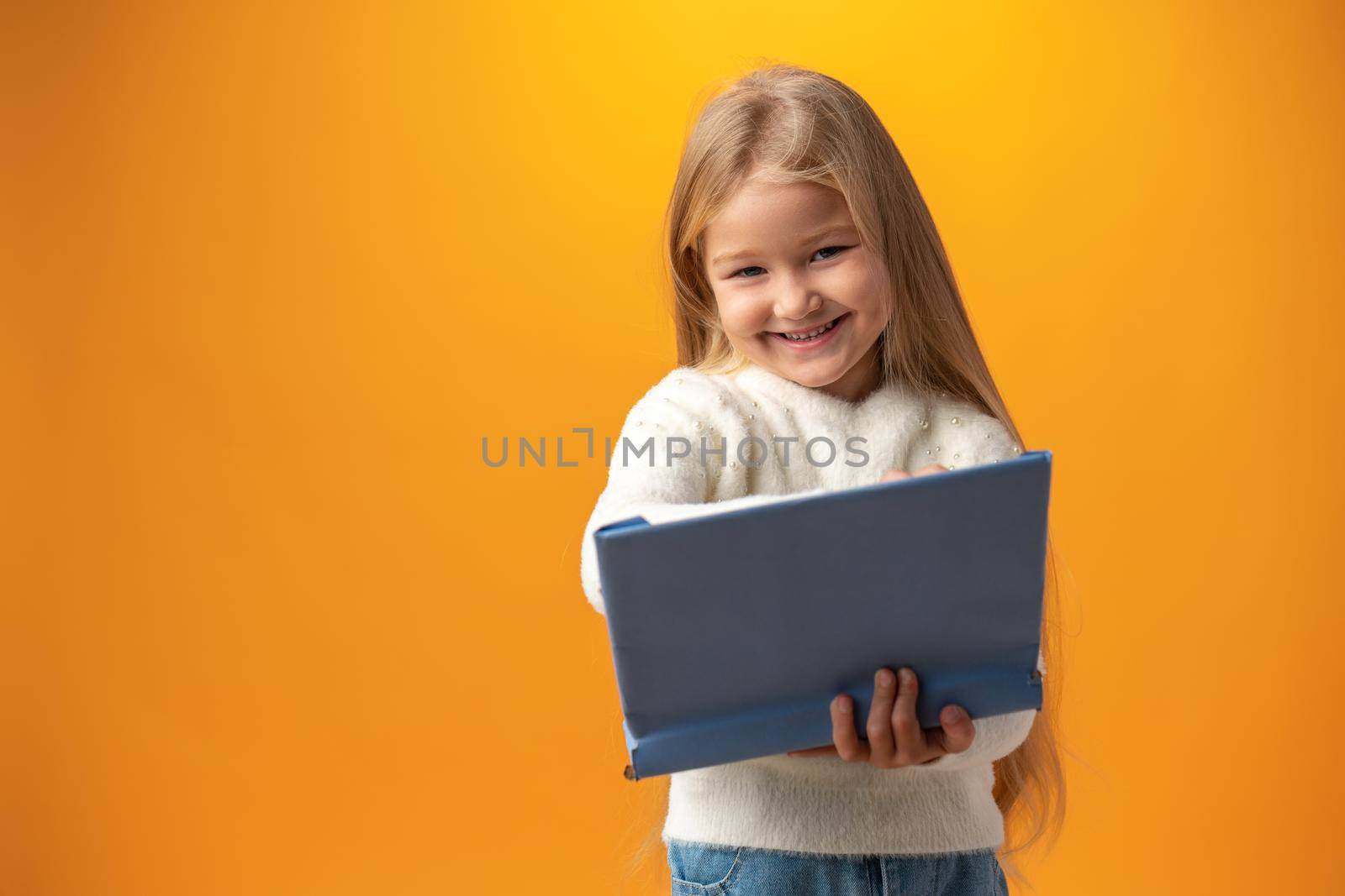 Portrait of little cute girl making notes against yellow background, close up