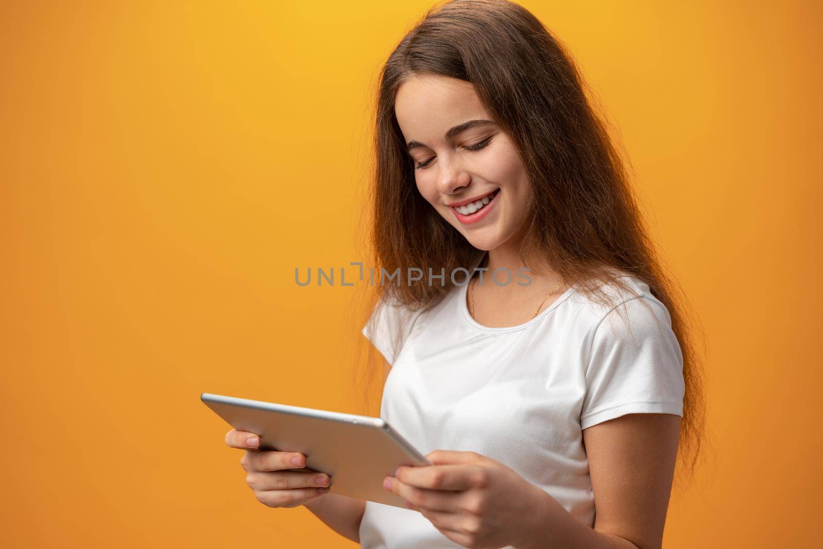 Beautiful teen girl using digital tablet over yellow studio background, close up