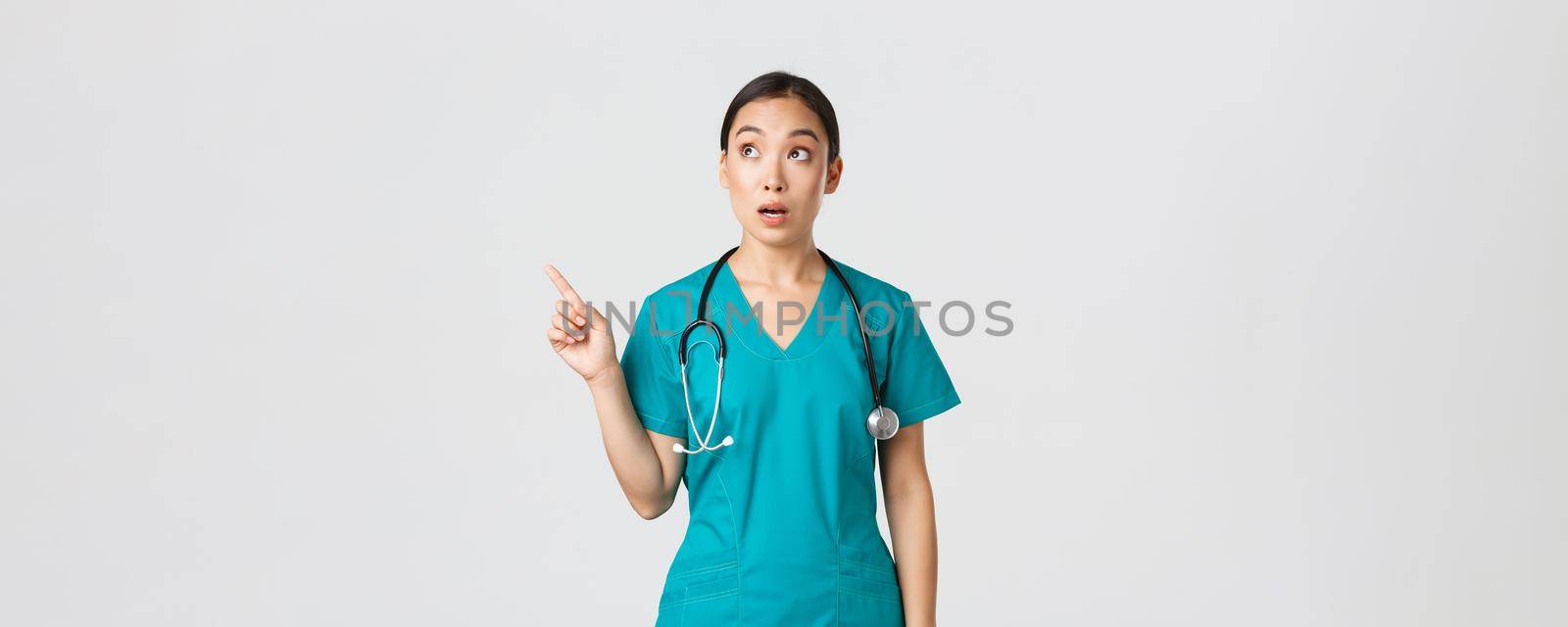 Covid-19, healthcare workers, pandemic concept. Surprised and amazed female asian physician looking and pointing upper left corner. Astonished korean doctor stare at banner with advertisement by Benzoix