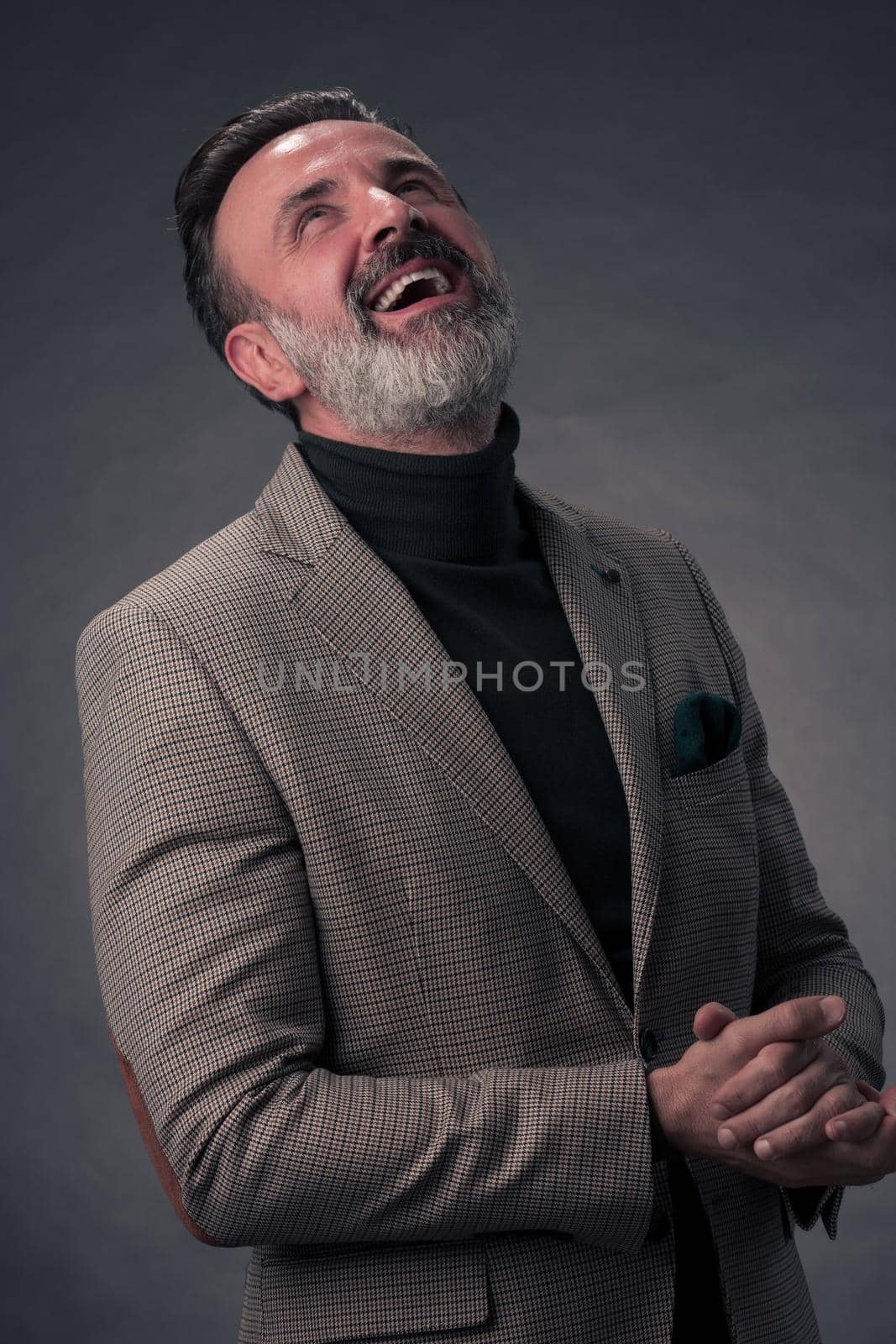 Portrait of a stylish elegant senior businessman with a beard and casual business clothes in photo studio isolated on dark background gesturing with hands. High quality photo