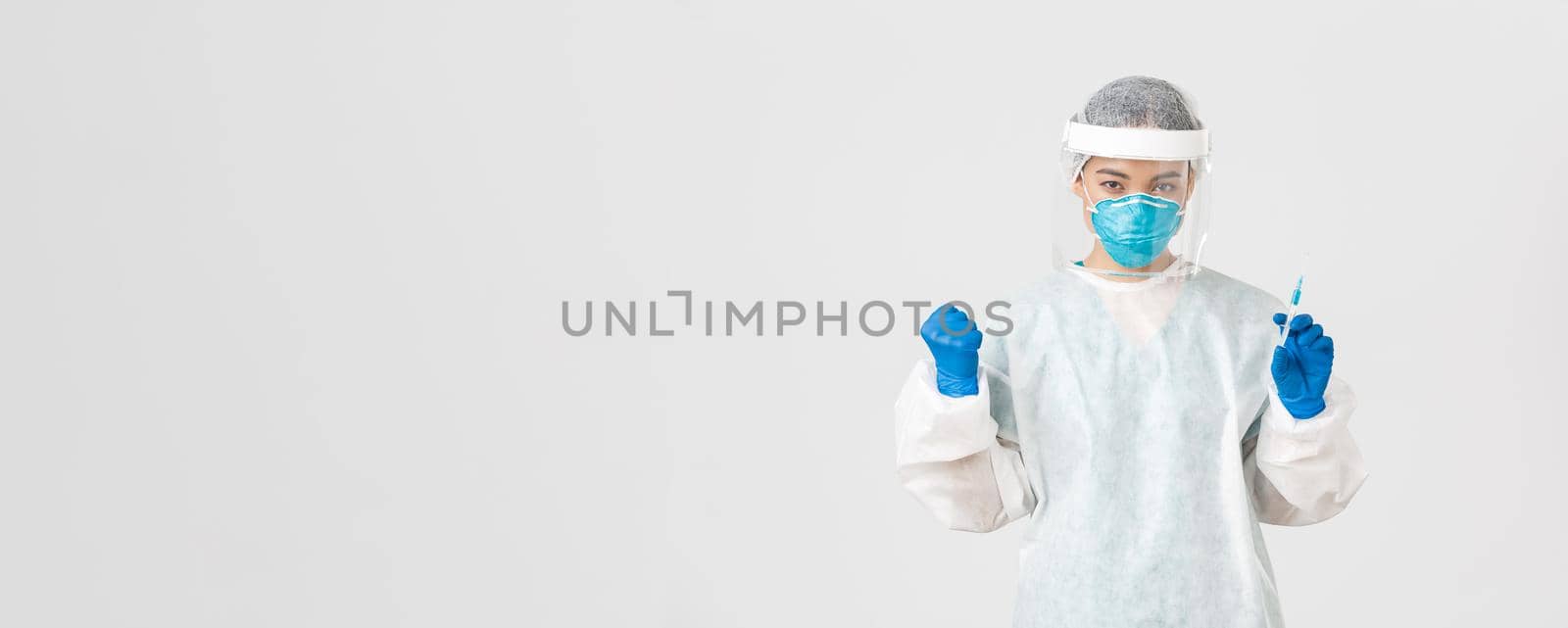 Covid-19, coronavirus disease, healthcare workers concept. Determined and confident female asian doctor, tech lab employee in personal protective equipment holding syringe with vaccine by Benzoix