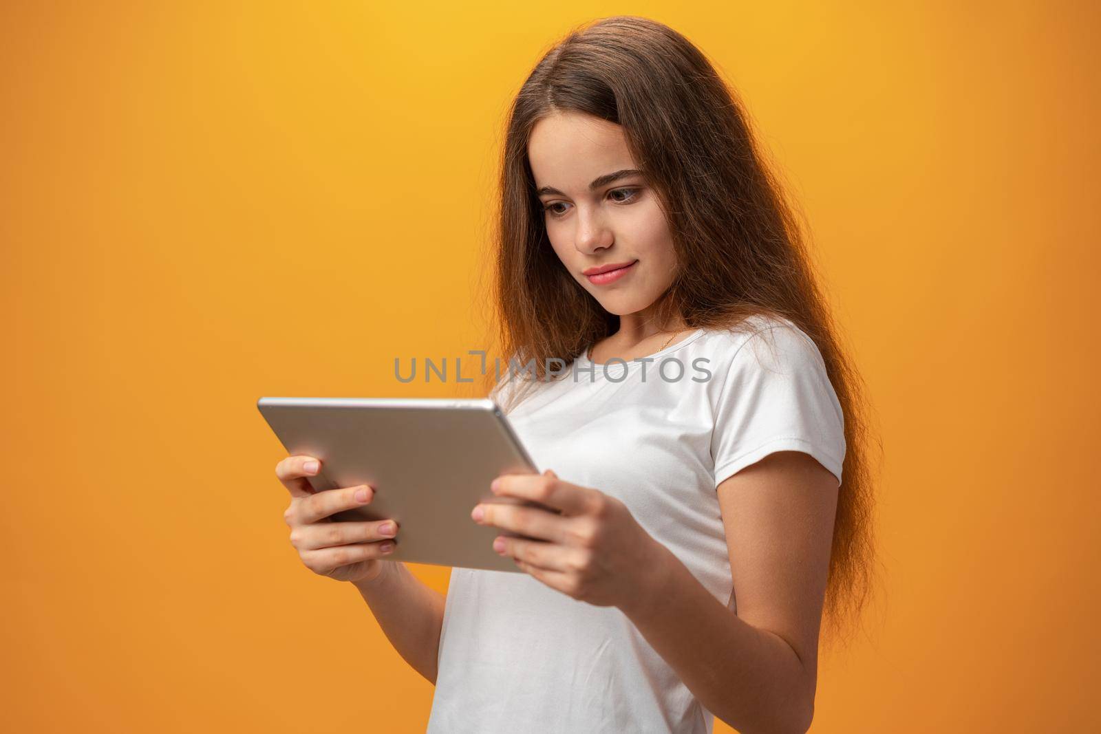 Beautiful teen girl using digital tablet over yellow studio background, close up