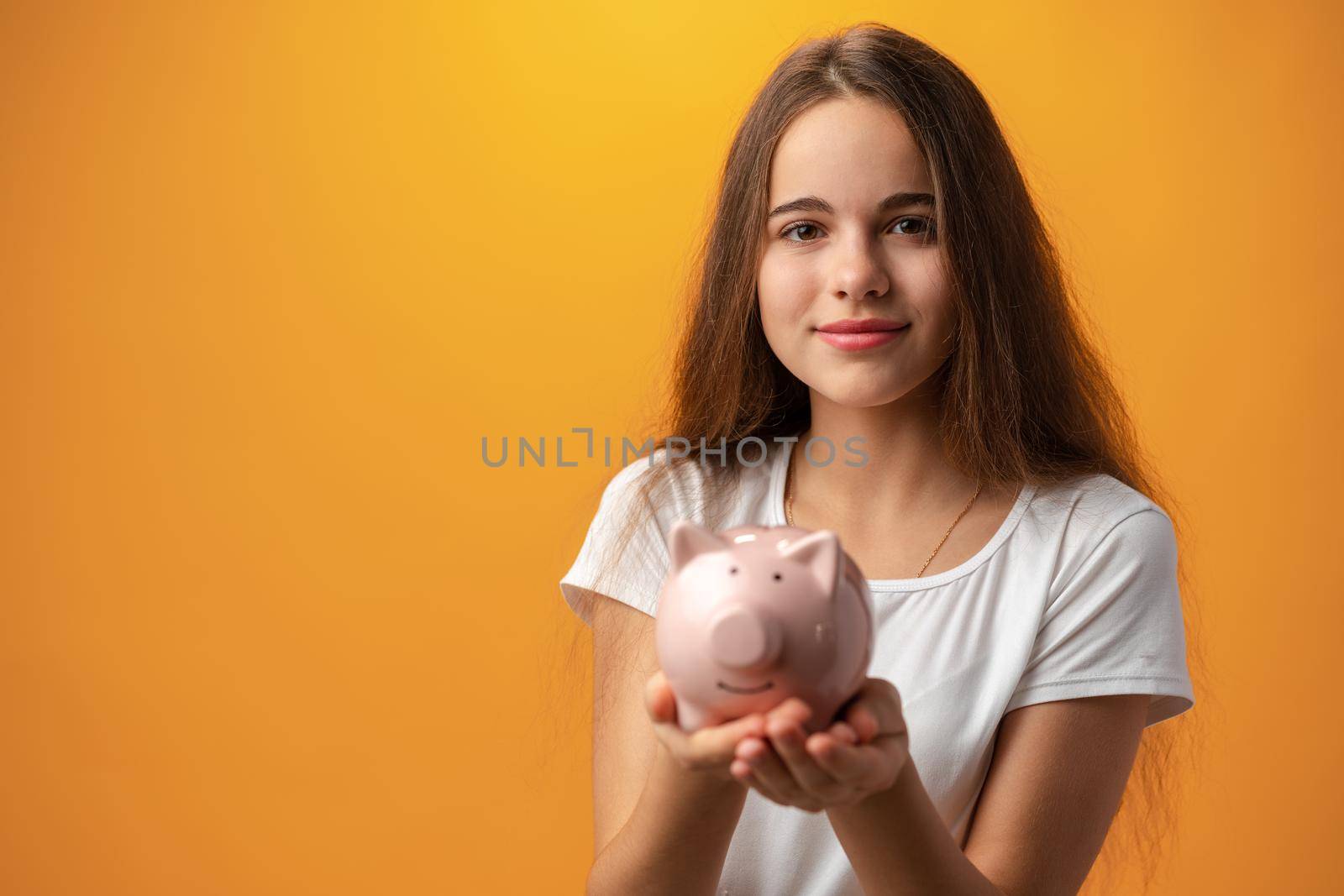 Teen girl with piggy bank on yellow background, close up