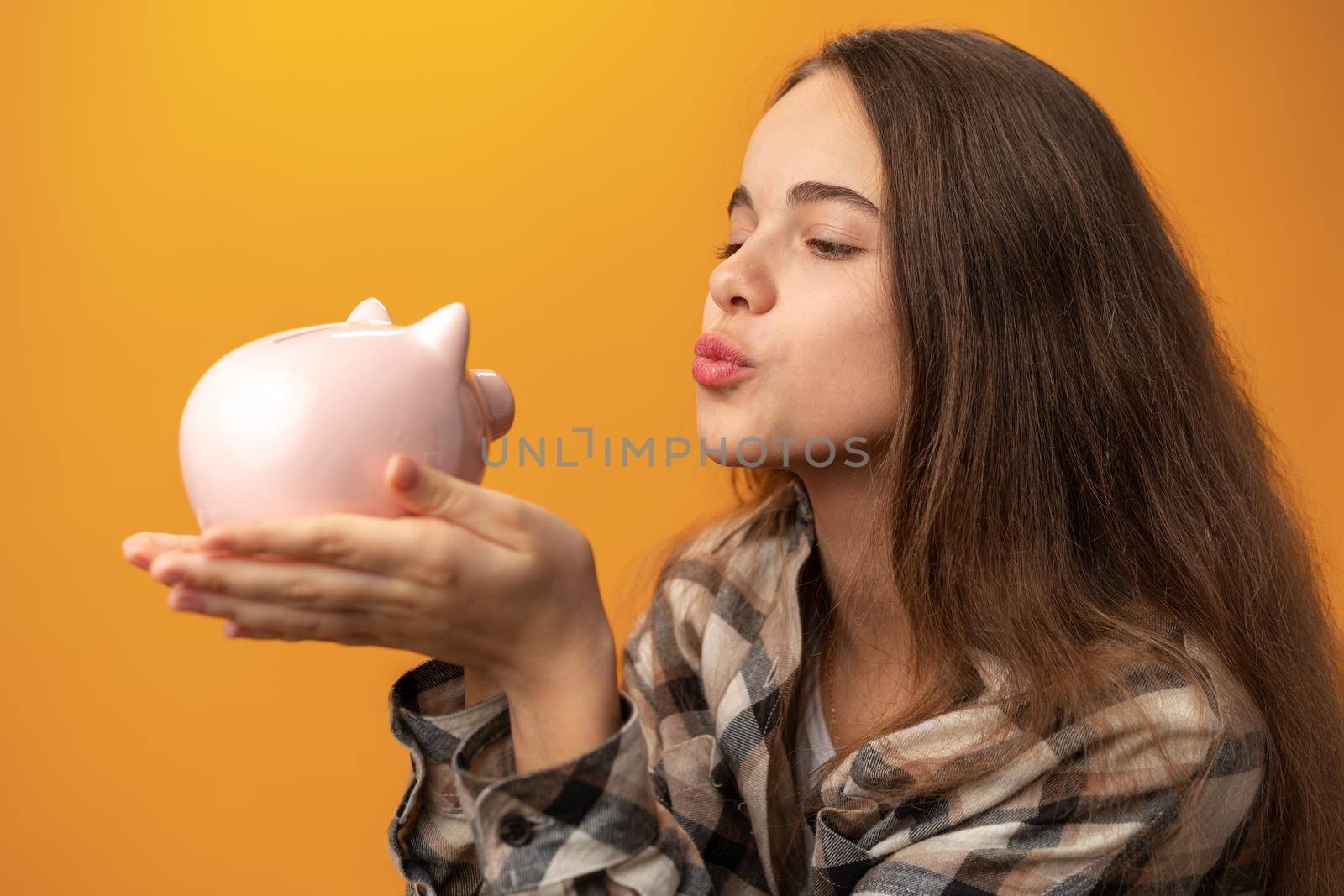 Teen girl with piggy bank on yellow background, close up