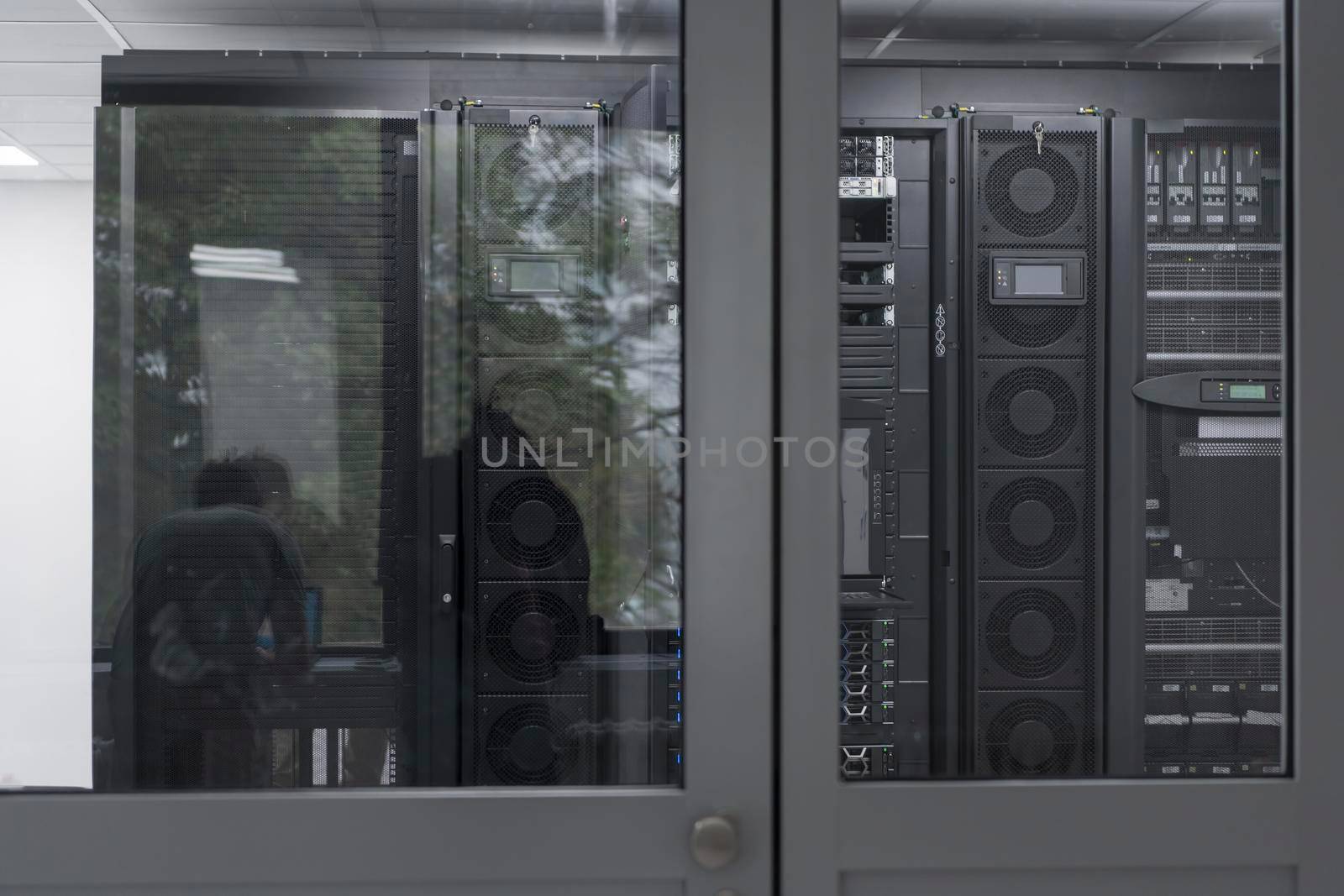 Software Engineer Working on a Laptop Computer in a Modern Server room. Monitoring Room Big Data Scientist in reflection of the entrance door. by dotshock