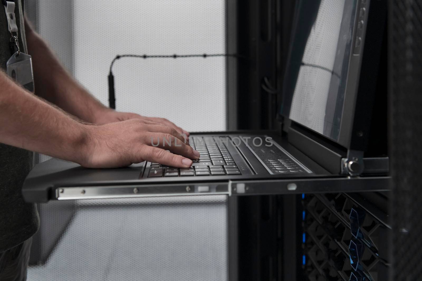 Close up on Data Center Engineer hands Using keyboard on a supercomputer Server Room Specialist Facility with Male System Administrator Working with Data Protection Network for Cyber Security. by dotshock