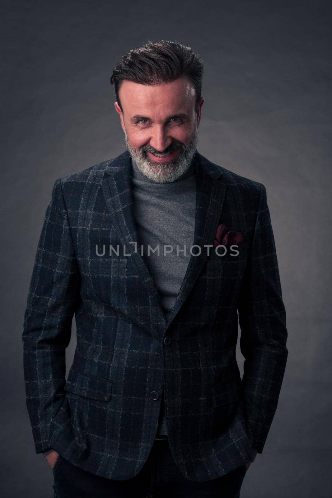 Portrait of a stylish elegant senior businessman with a beard and casual business clothes in photo studio isolated on dark background gesturing with hands. High quality photo