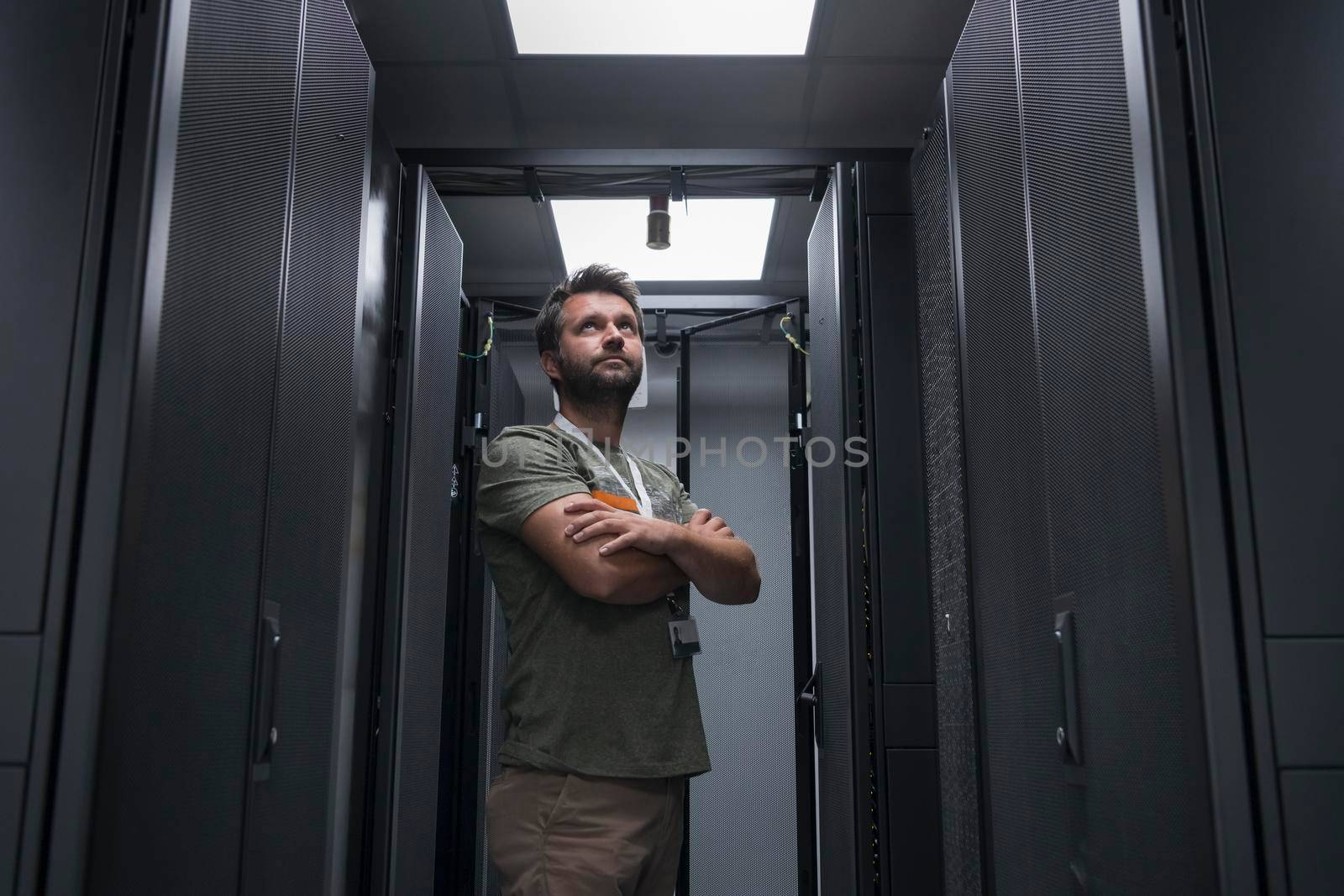 Portrait of male technician or network administrator standing brave as a hero with arms crossed in data center server room. High quality photo