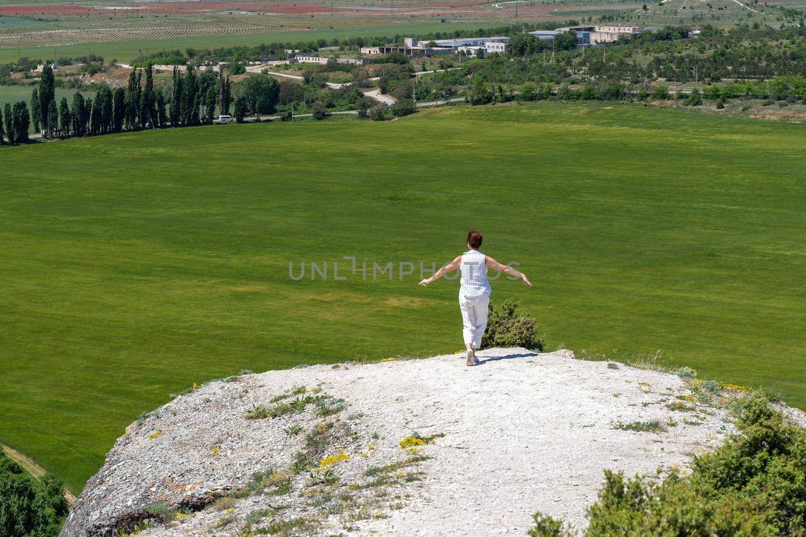 The woman at the top of the mountain raised her hands up on blue sky background. The woman climbed to the top and enjoyed her success. Back view