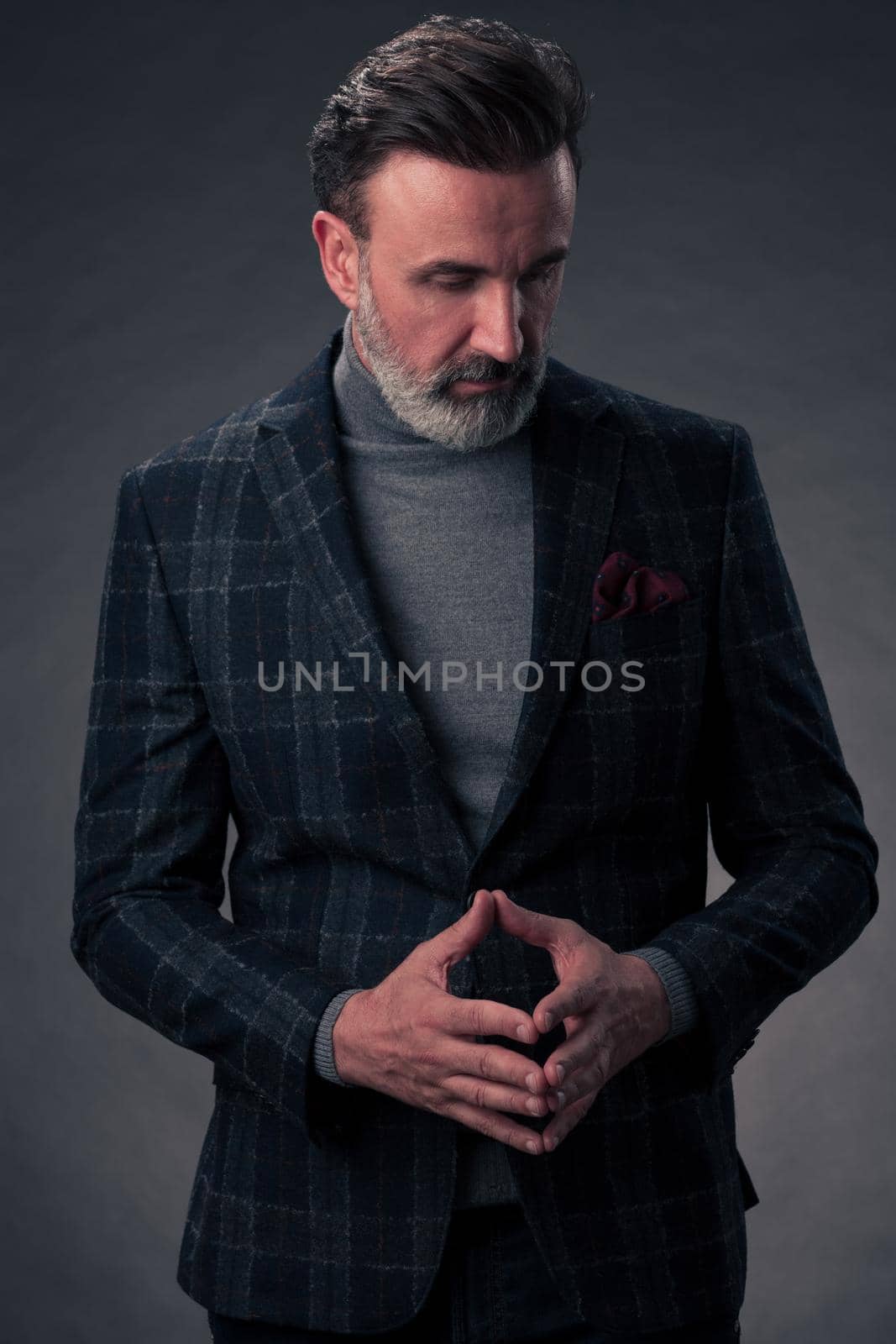 Portrait of a stylish elegant senior businessman with a beard and casual business clothes in photo studio isolated on dark background gesturing with hands. High quality photo