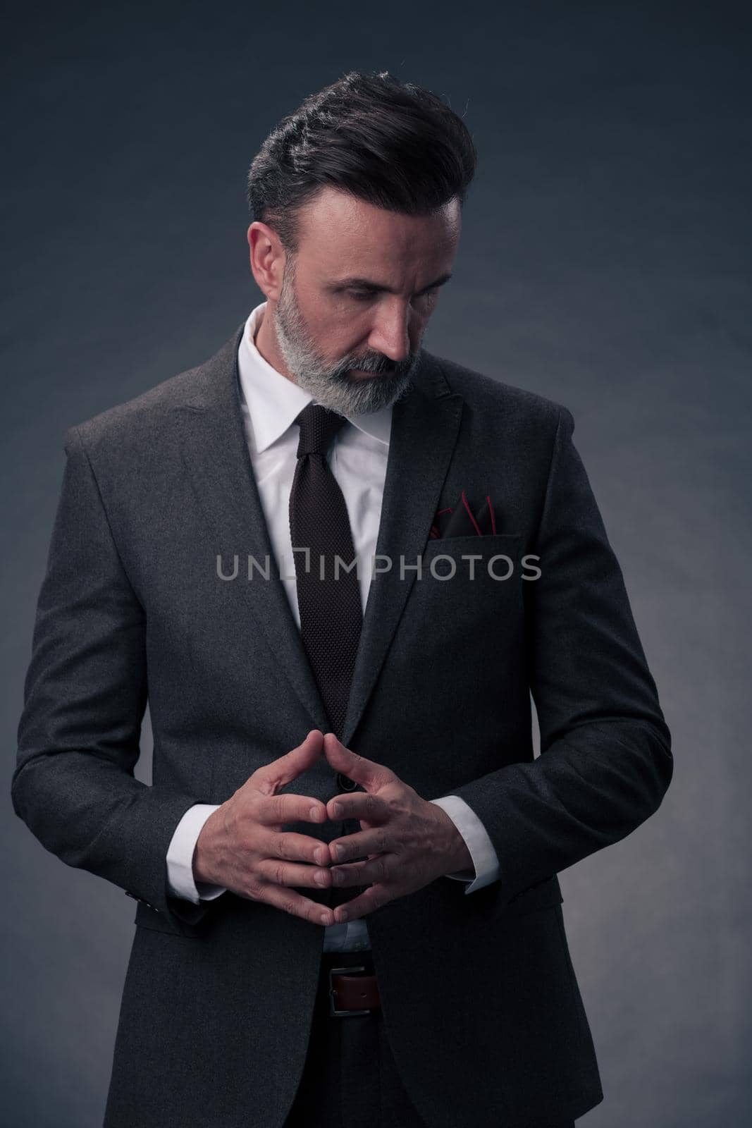 Portrait of a stylish elegant senior businessman with a beard and casual business clothes in photo studio isolated on dark background gesturing with hands. High quality photo