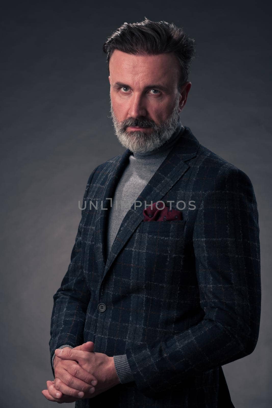 Portrait of a stylish elegant senior businessman with a beard and casual business clothes in photo studio isolated on dark background gesturing with hands by dotshock