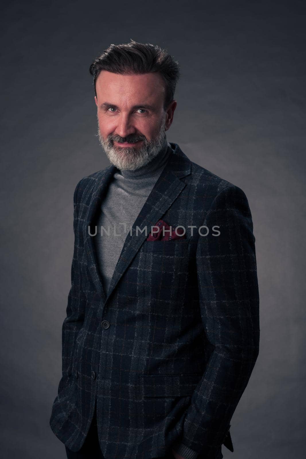 Portrait of a stylish elegant senior businessman with a beard and casual business clothes in photo studio isolated on dark background gesturing with hands. High quality photo