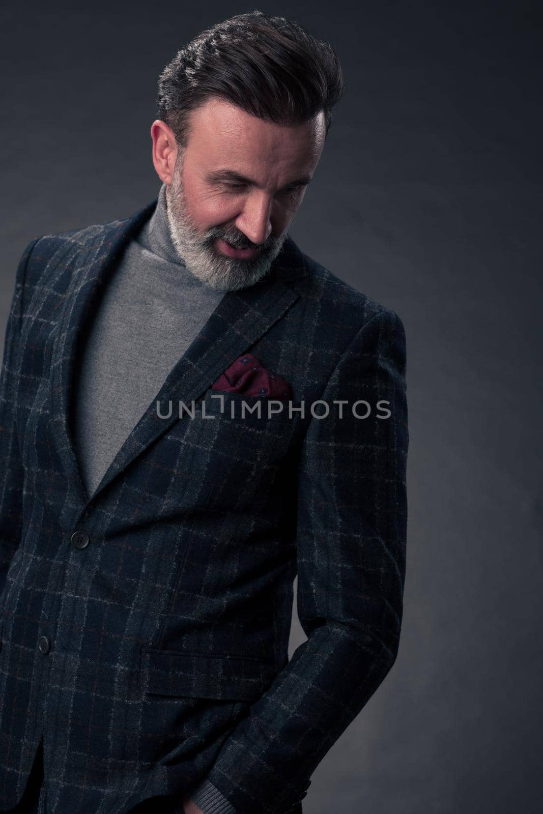 Portrait of a stylish elegant senior businessman with a beard and casual business clothes in photo studio isolated on dark background gesturing with hands. High quality photo