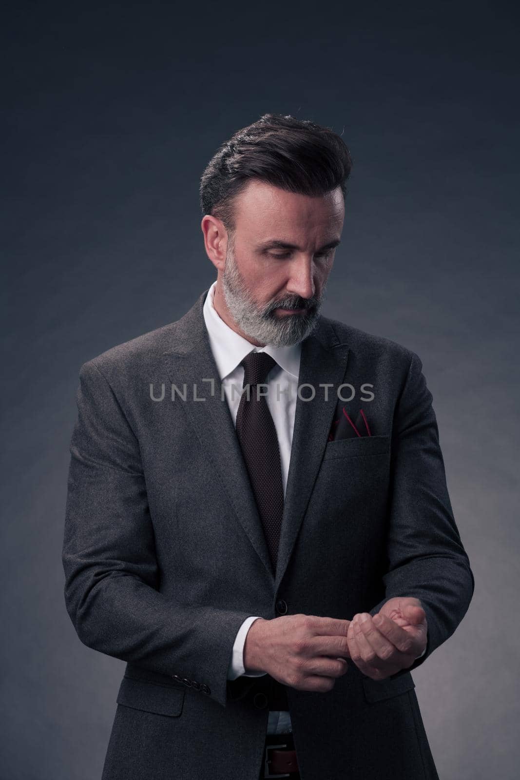 Portrait of a stylish elegant senior businessman with a beard and casual business clothes in photo studio isolated on dark background gesturing with hands. High quality photo