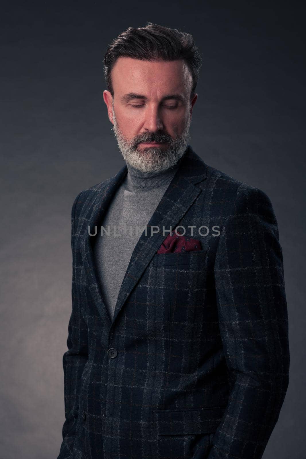 Portrait of a stylish elegant senior businessman with a beard and casual business clothes in photo studio isolated on dark background gesturing with hands. High quality photo