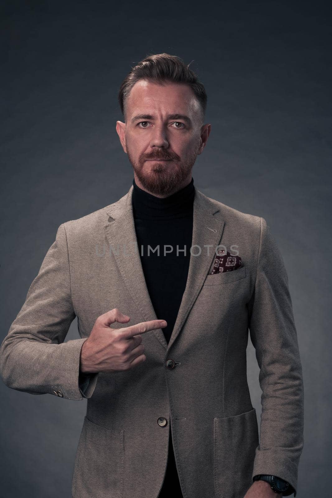 Portrait of a stylish elegant senior businessman with a beard and casual business clothes in photo studio isolated on dark background gesturing with hands. High quality photo