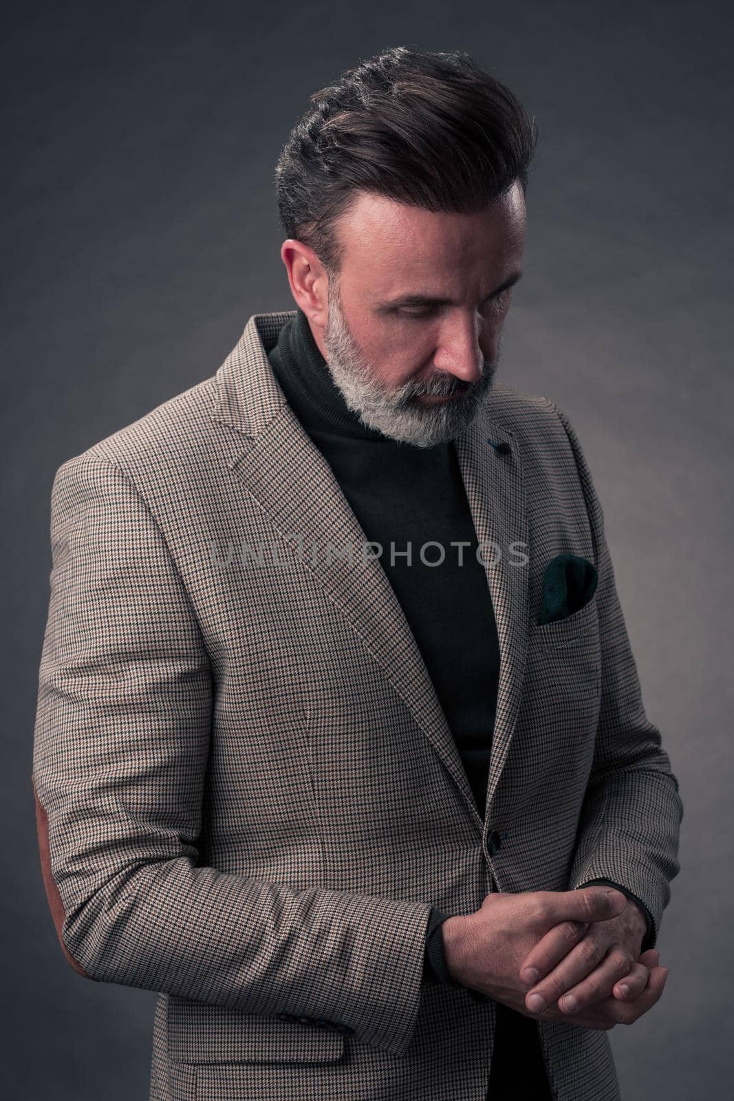 Portrait of a stylish elegant senior businessman with a beard and casual business clothes in photo studio isolated on dark background gesturing with hands. High quality photo