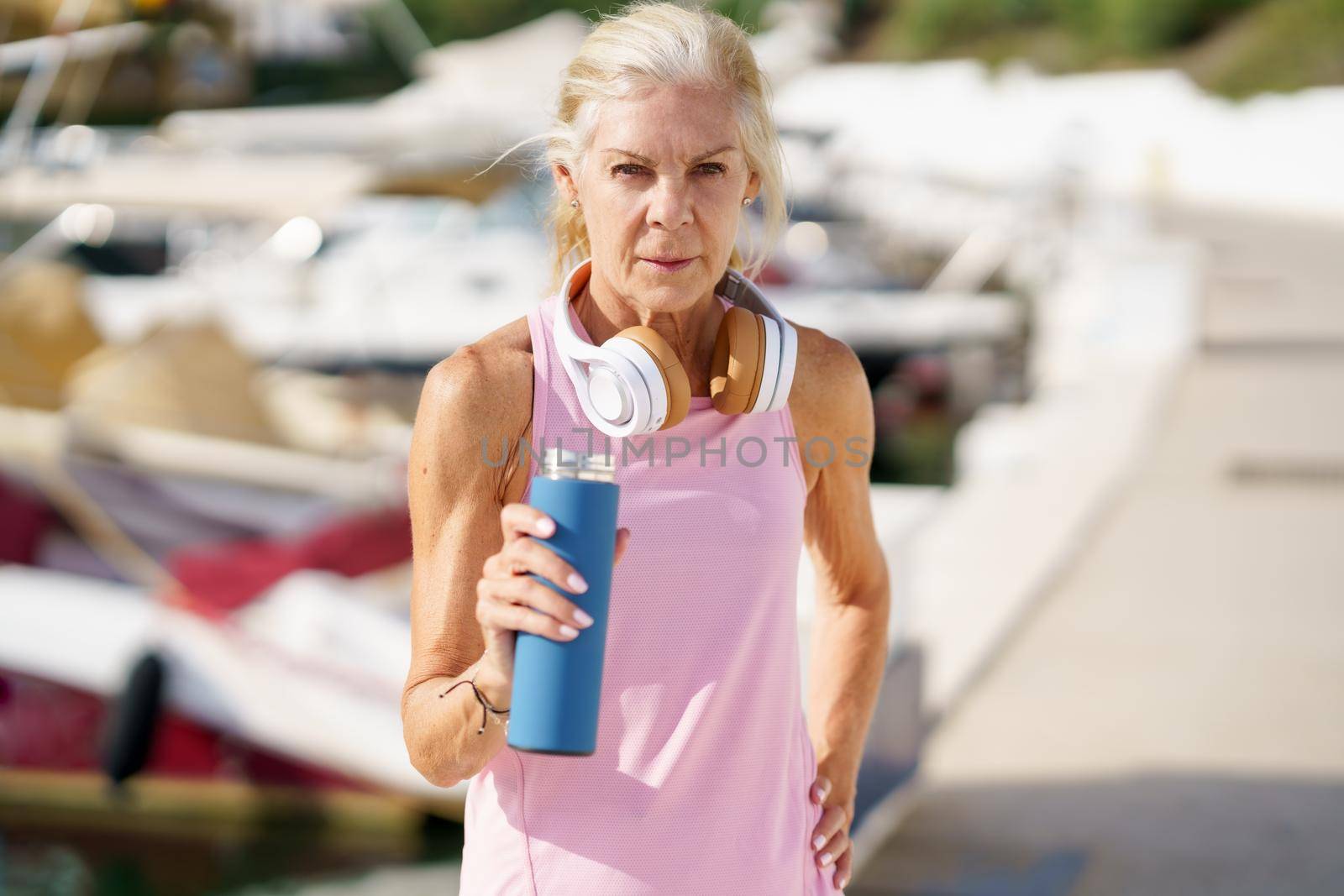 Mature sportswoman taking a break during exercise to hydrate herself. Senior woman in fitness clothing drinking water from a metal fitness bottle. Concept of healthy living in the elderly.