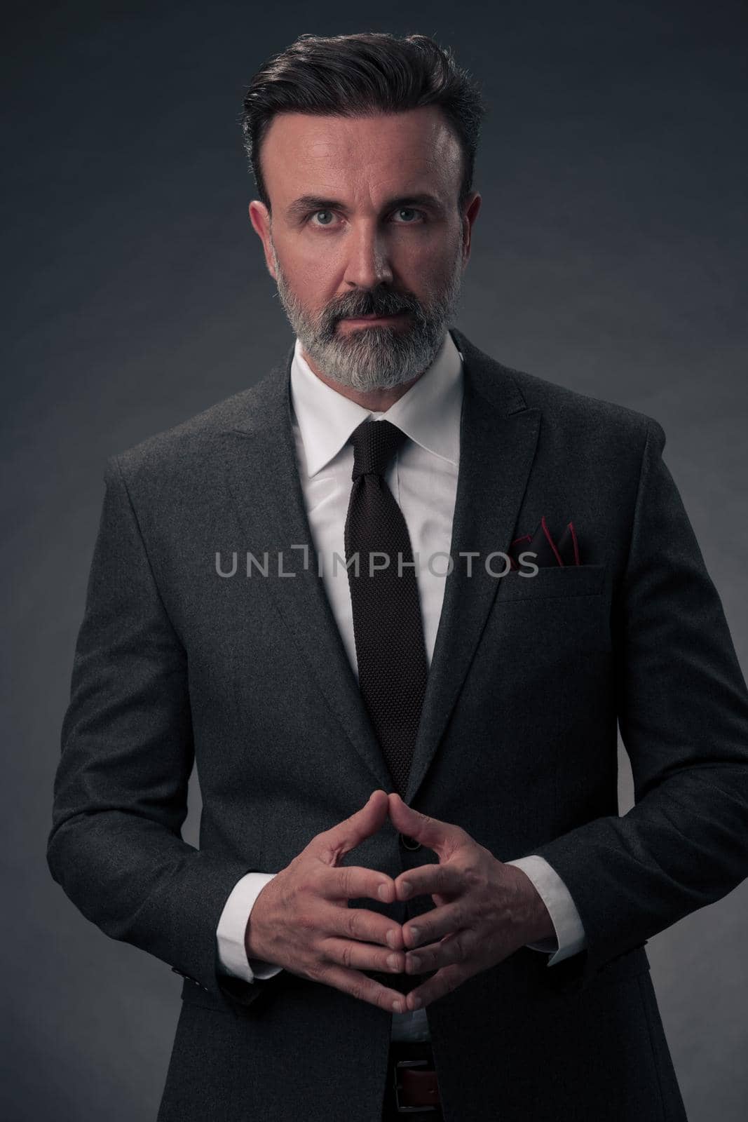 Portrait of a stylish elegant senior businessman with a beard and casual business clothes in photo studio isolated on dark background gesturing with hands. High quality photo