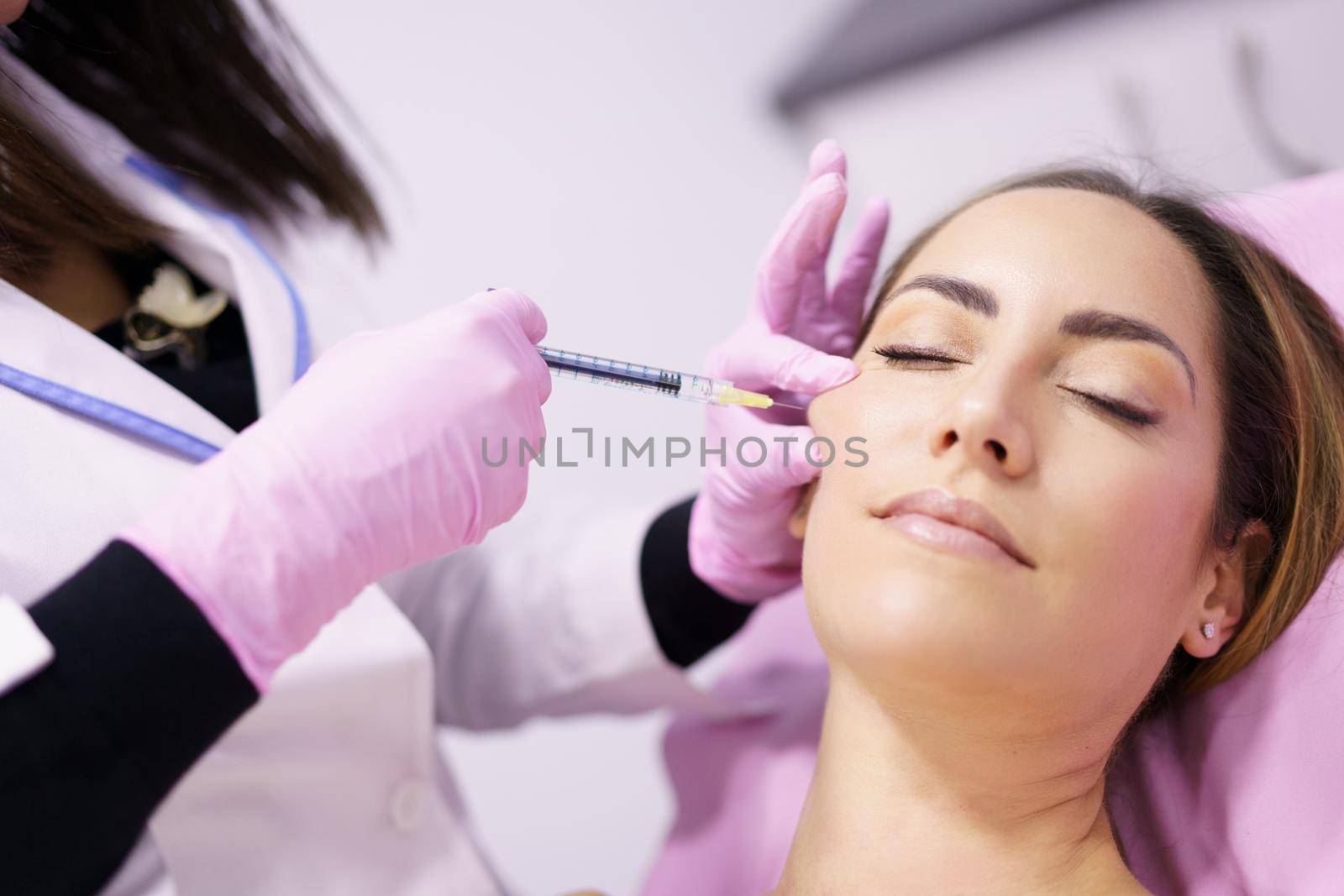 Doctor injecting hyaluronic acid into the cheekbones of a woman as a facial rejuvenation treatment. by javiindy
