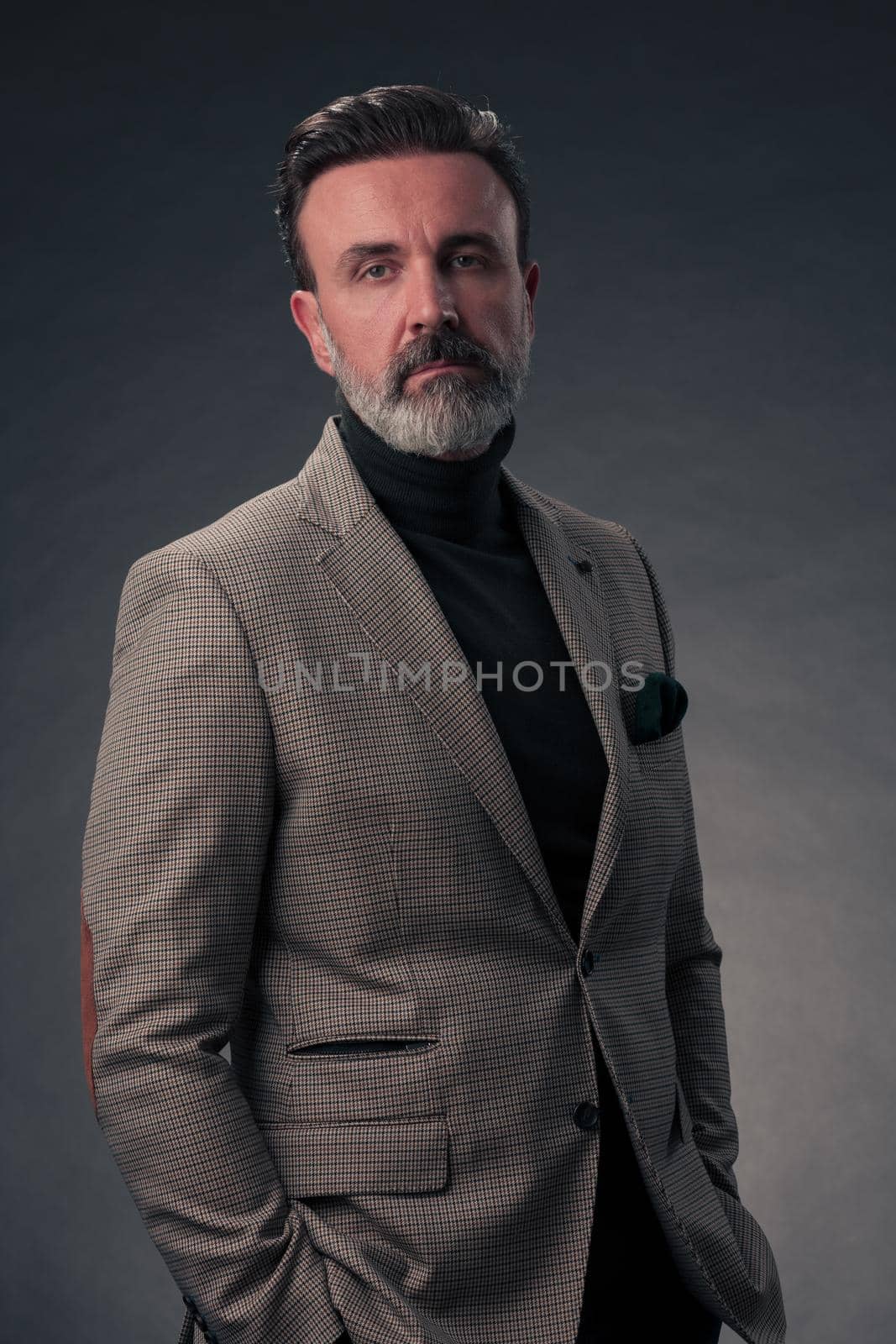 Portrait of a stylish elegant senior businessman with a beard and casual business clothes in photo studio isolated on dark background gesturing with hands. High quality photo