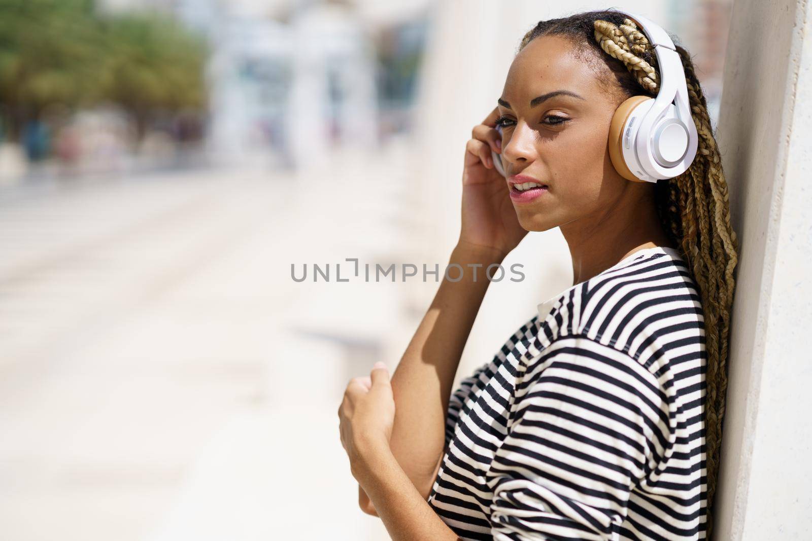 Beautiful young black woman listening to music with wireless headphones outdoors.