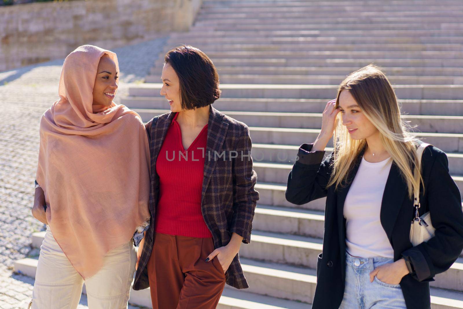 Positive young diverse female friends walking downstairs in campus by javiindy