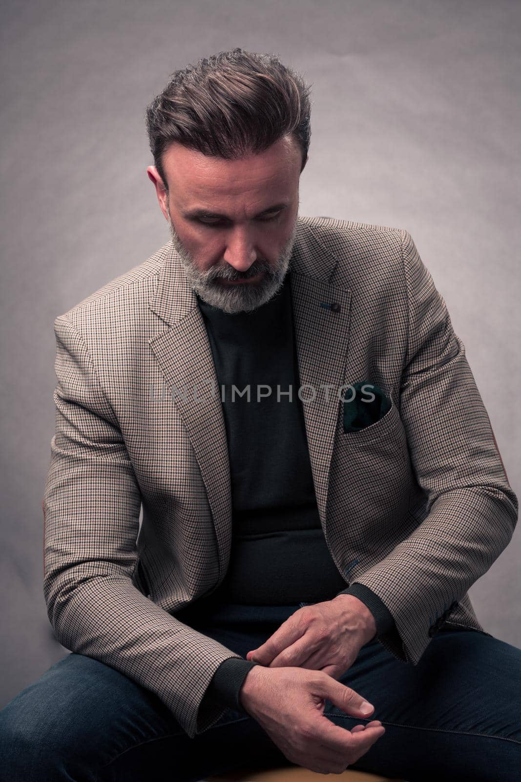 Portrait of a stylish elegant senior businessman with a beard and casual business clothes in photo studio isolated on dark background adjusting the suit