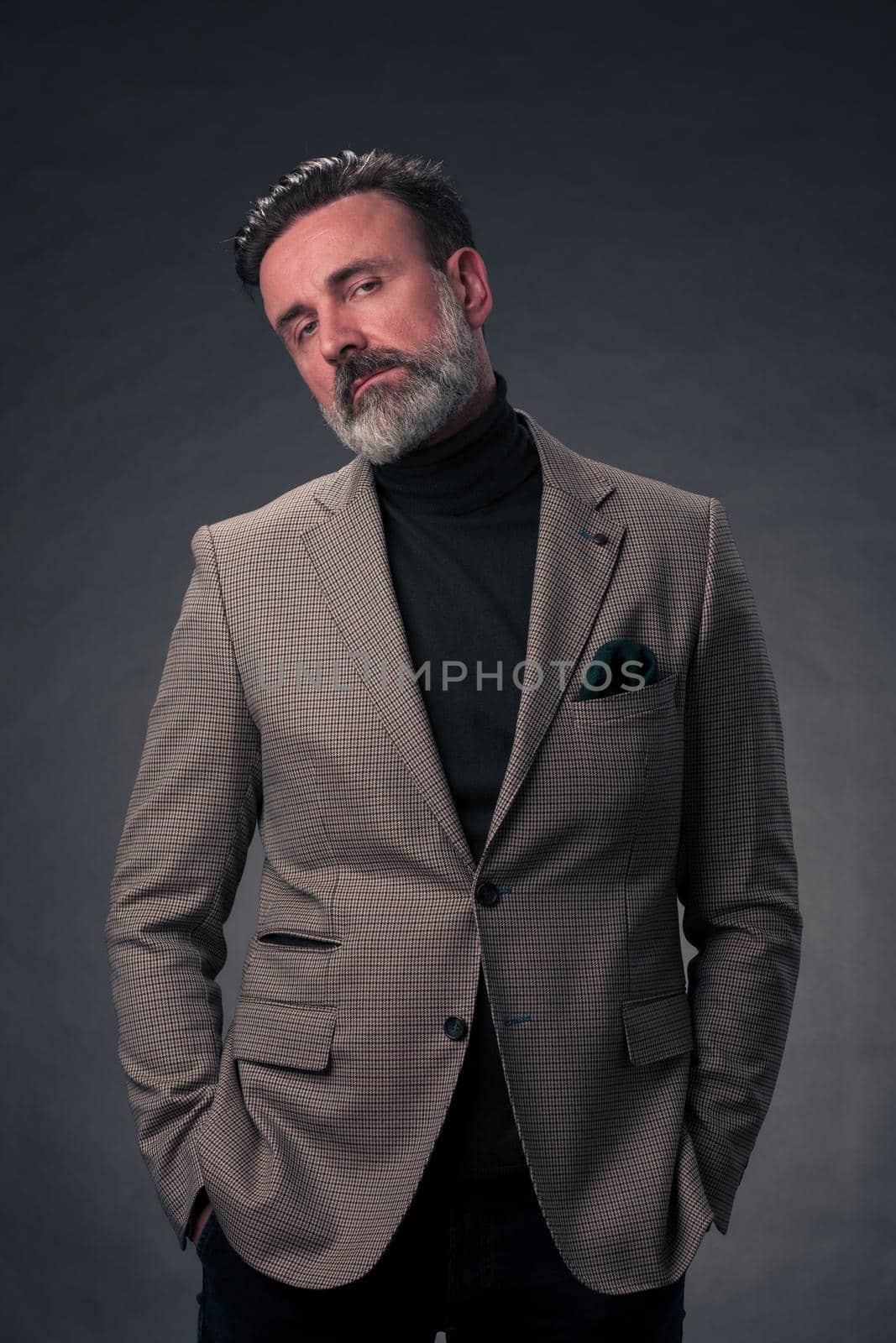 Portrait of a stylish elegant senior businessman with a beard and casual business clothes in photo studio isolated on dark background gesturing with hands. High quality photo