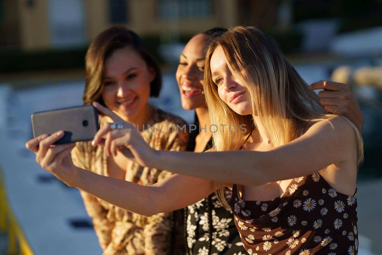 Woman taking self portrait on cellphone with positive young multiethnic girlfriends while enjoying time together