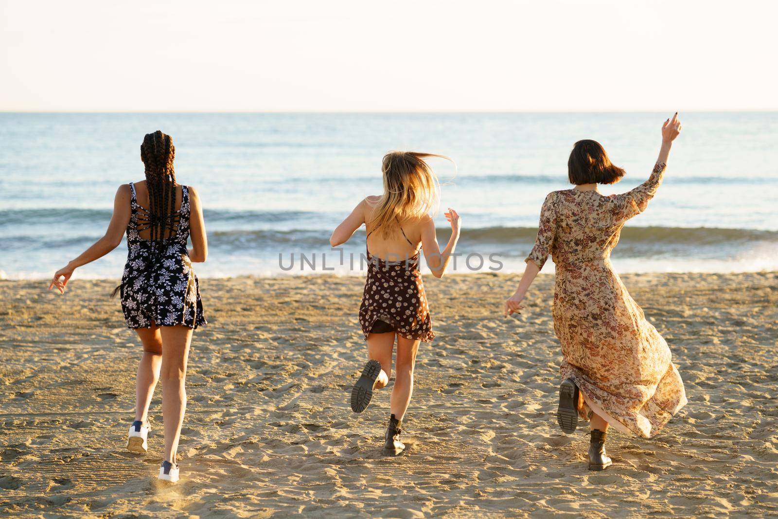 Girlfriends in summer dresses running towards waving sea by javiindy