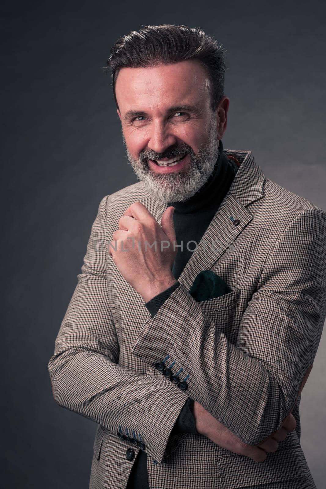 Portrait of a stylish elegant senior businessman with a beard and casual business clothes in photo studio isolated on dark background gesturing with hands. High quality photo