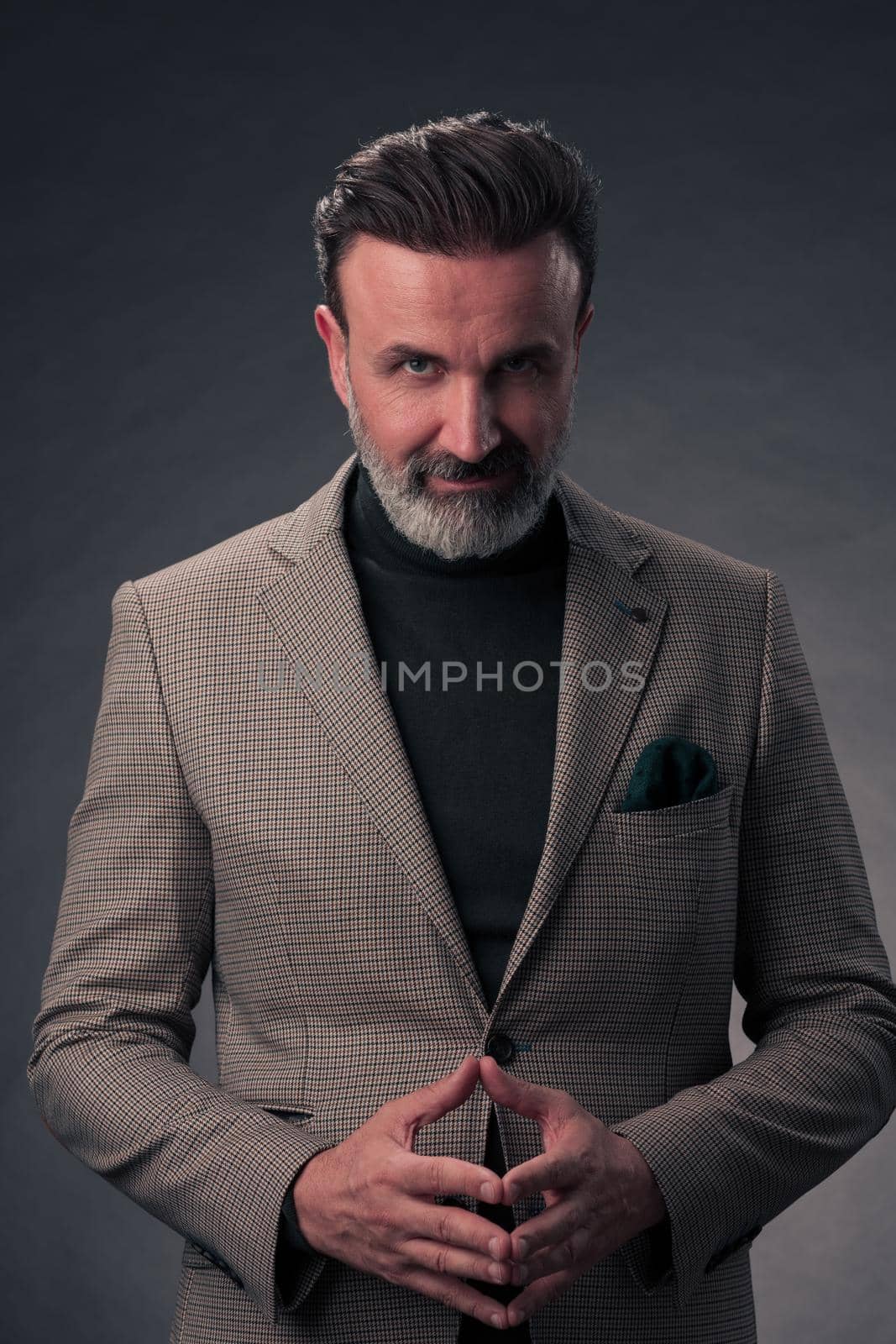 Portrait of a stylish elegant senior businessman with a beard and casual business clothes in photo studio isolated on dark background gesturing with hands by dotshock