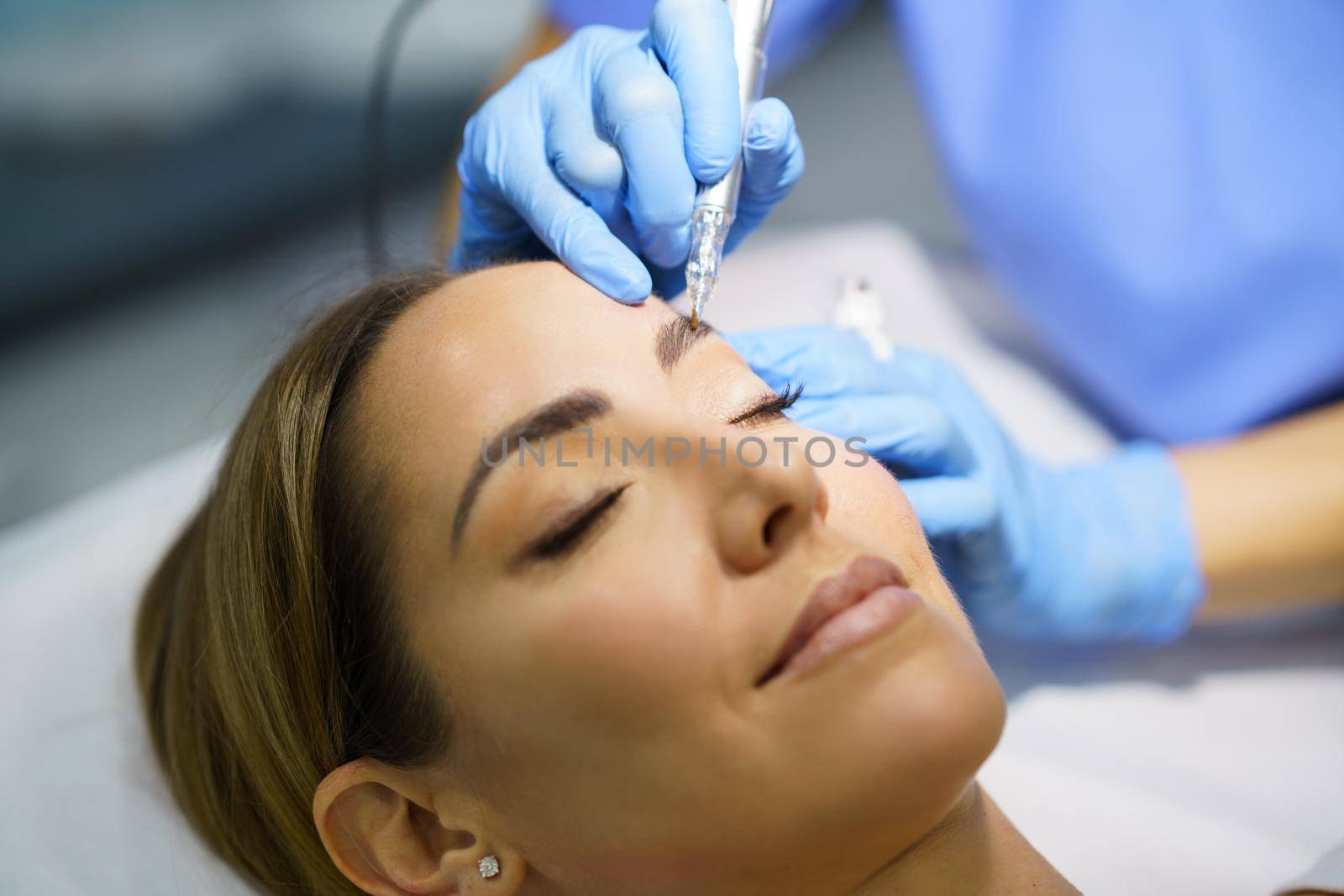 Permanent make-up for eyebrows of beautiful woman in a beauty salon. Close-up of beautician doing tattooing eyebrow. Micropigmentation treatment.