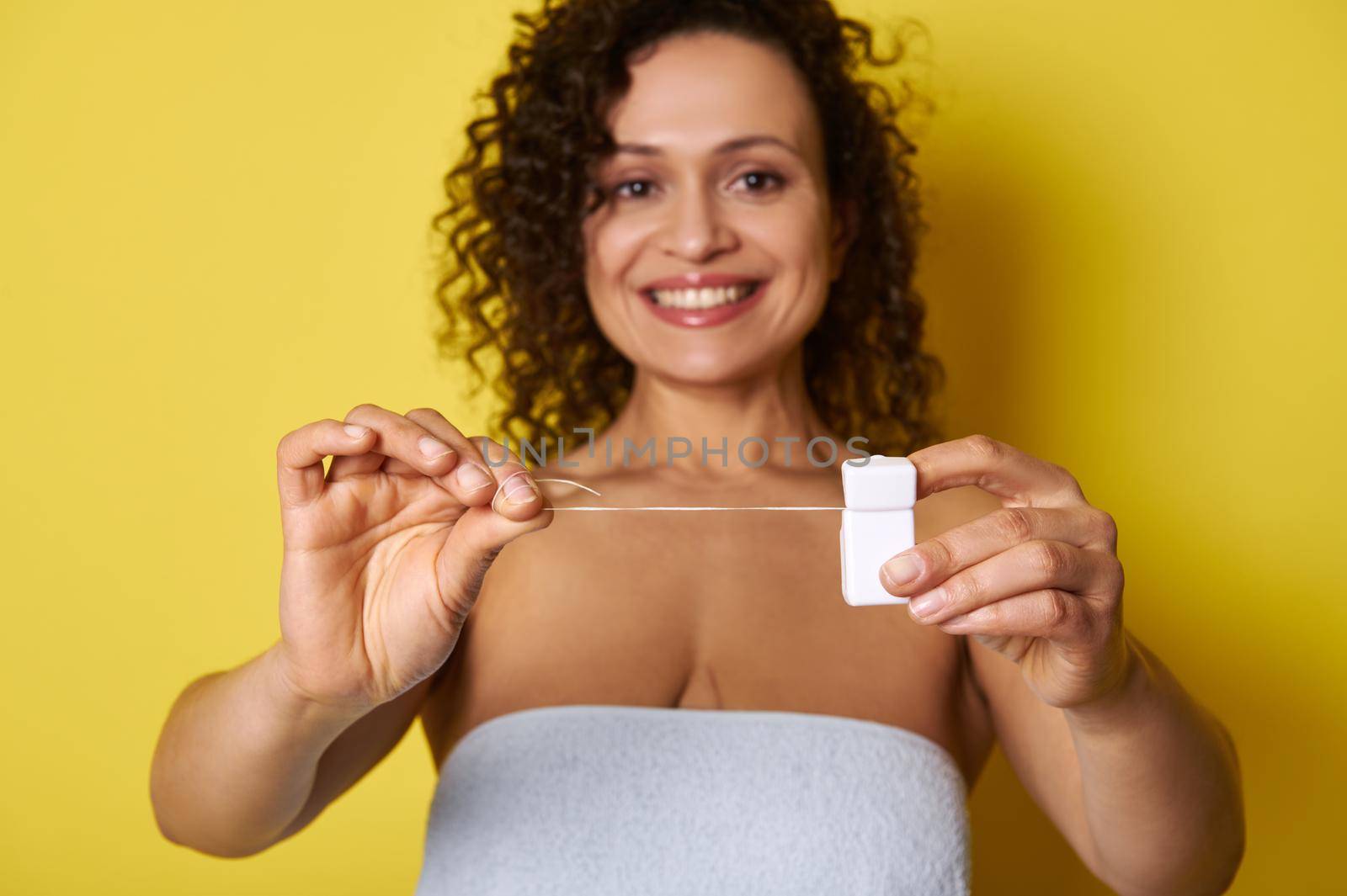 Soft focus on hygiene dental floss in hands of smiling woman with beautiful toothy smile, isolated on yellow background with copy space