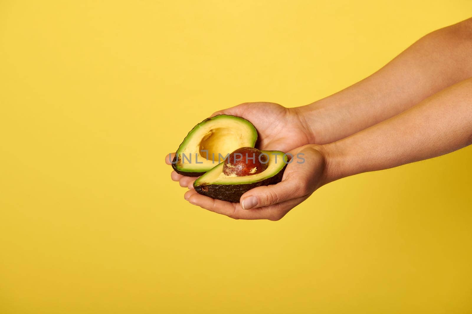 Closeup of hands holding two halves of ripe ready-to-eat avocado by artgf