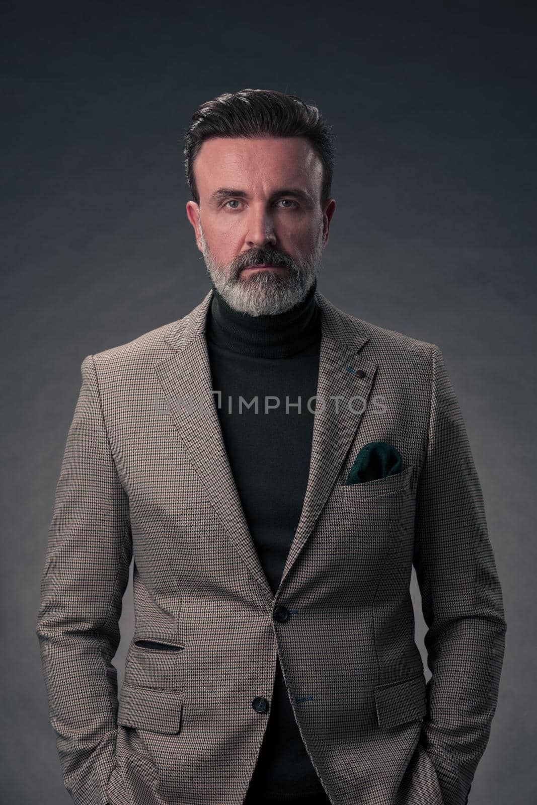 Portrait of a stylish elegant senior businessman with a beard and casual business clothes in photo studio isolated on dark background gesturing with hands. High quality photo