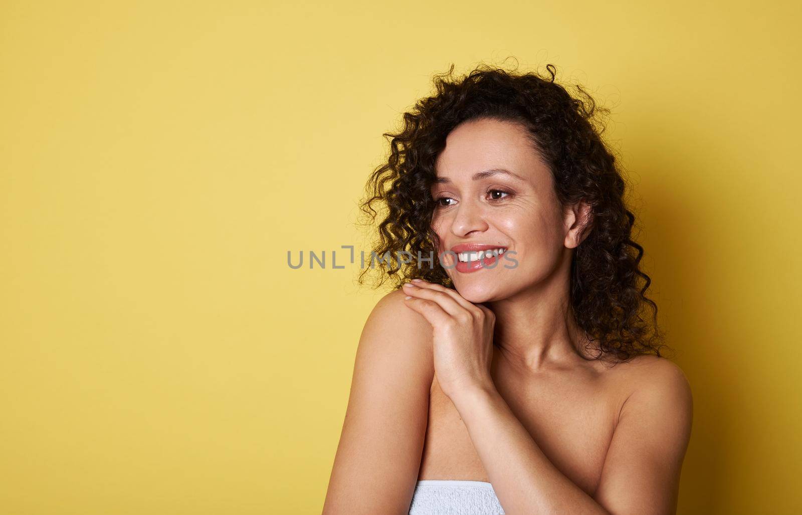 Attractive African American young woman with curly hair looking away and smiling with toothy smile. Yellow background. Copy space by artgf