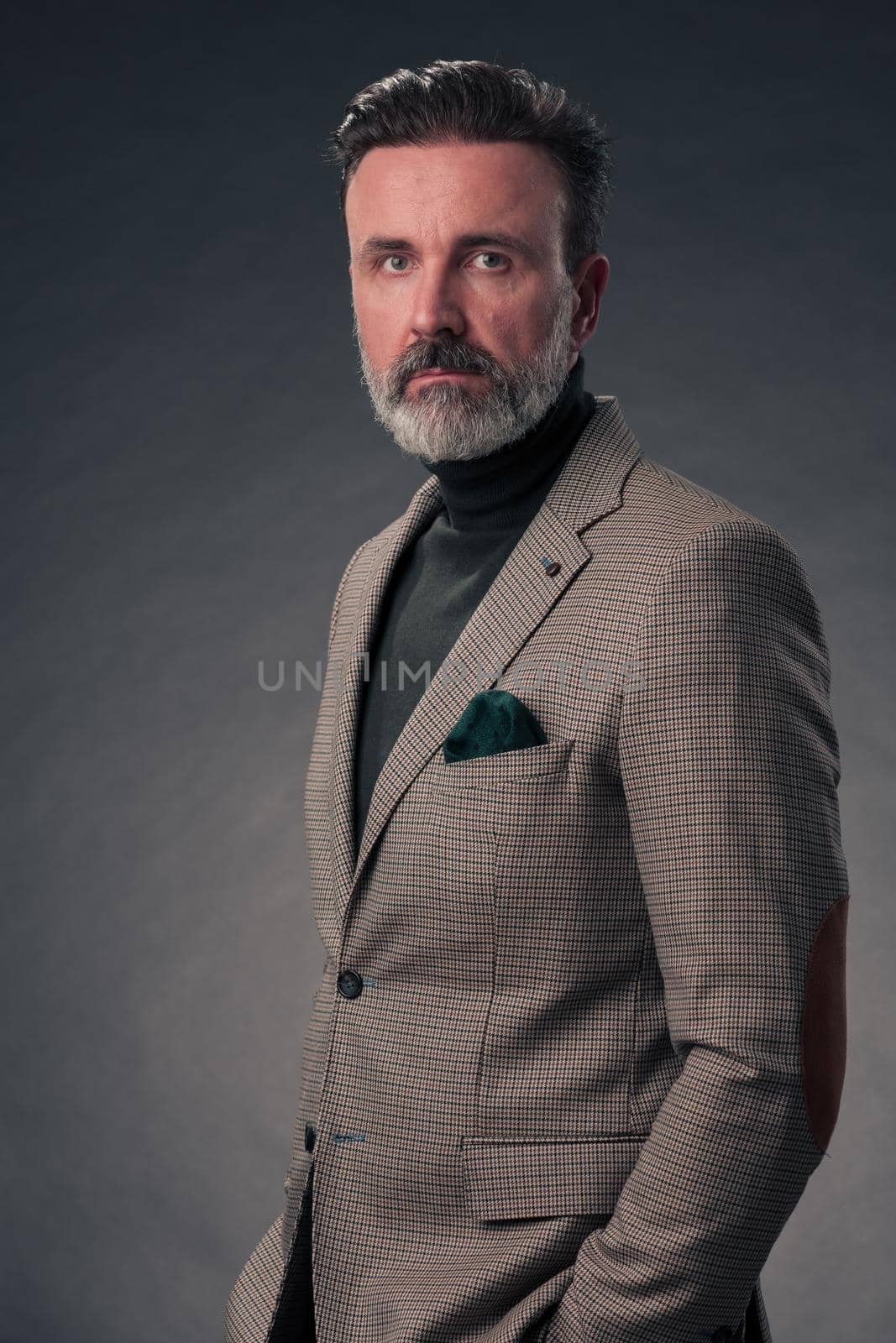 Portrait of a stylish elegant senior businessman with a beard and casual business clothes in photo studio isolated on dark background gesturing with hands. High quality photo