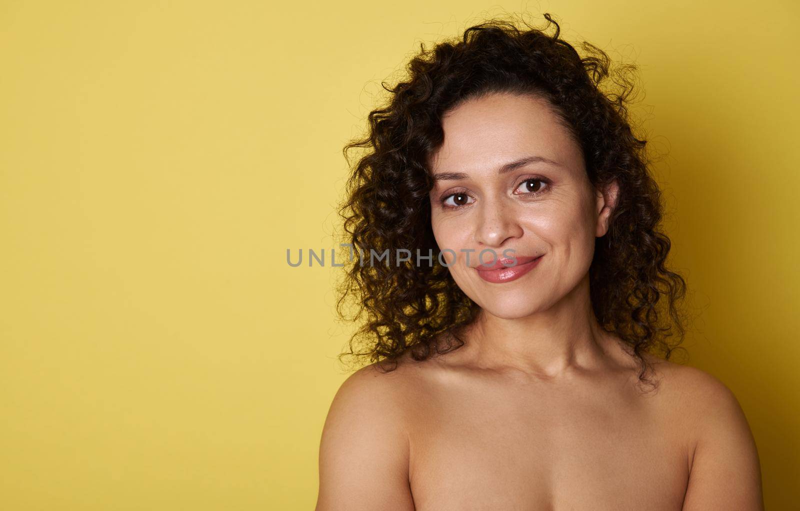 Young hispanic woman with curly hair cute smiling at the camera while standing on yellow background with copy space by artgf