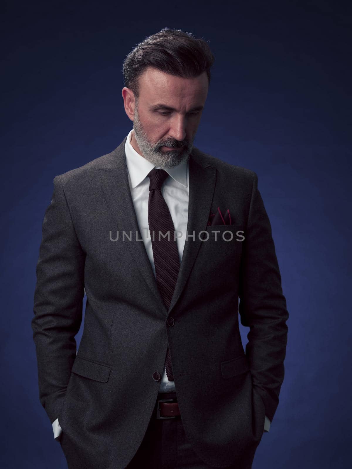 Portrait of a stylish elegant senior businessman with a beard and casual business clothes in photo studio isolated on dark background gesturing with hands. High quality photo