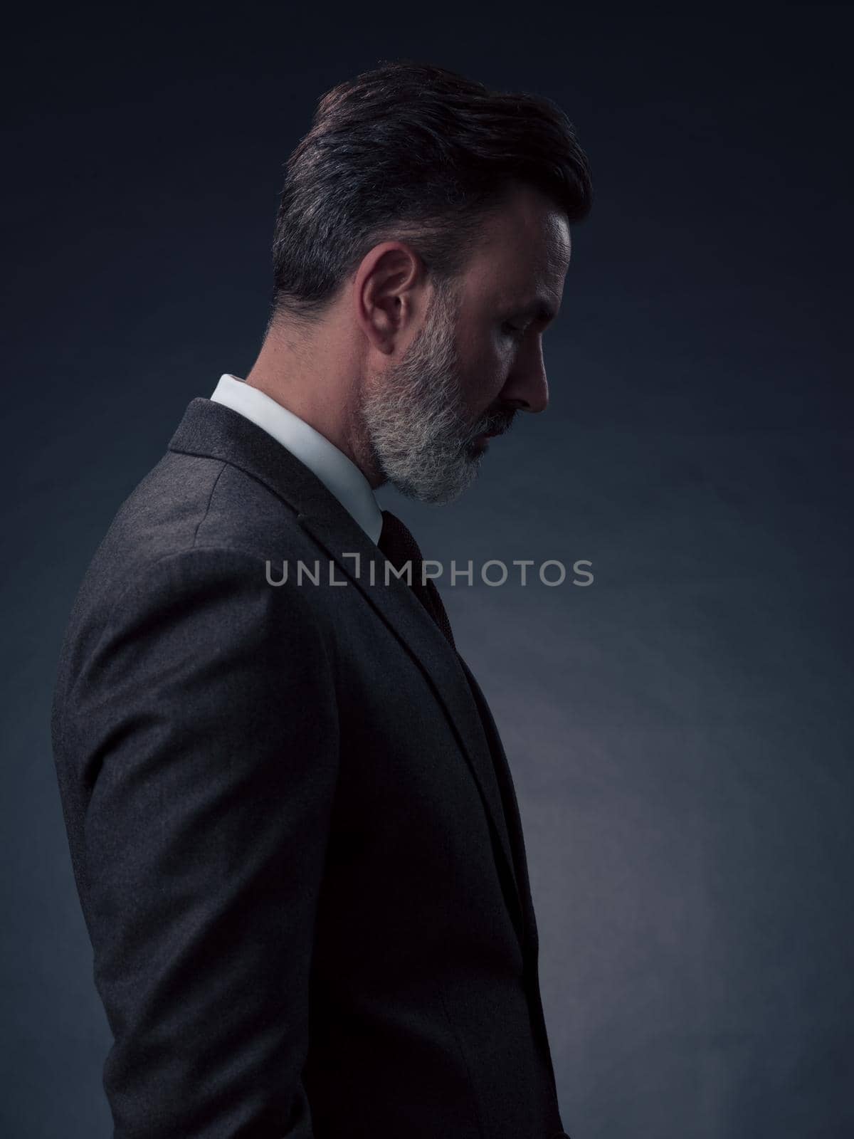 Portrait of a stylish elegant senior businessman with a beard and casual business clothes in photo studio isolated on dark background gesturing with hands. High quality photo