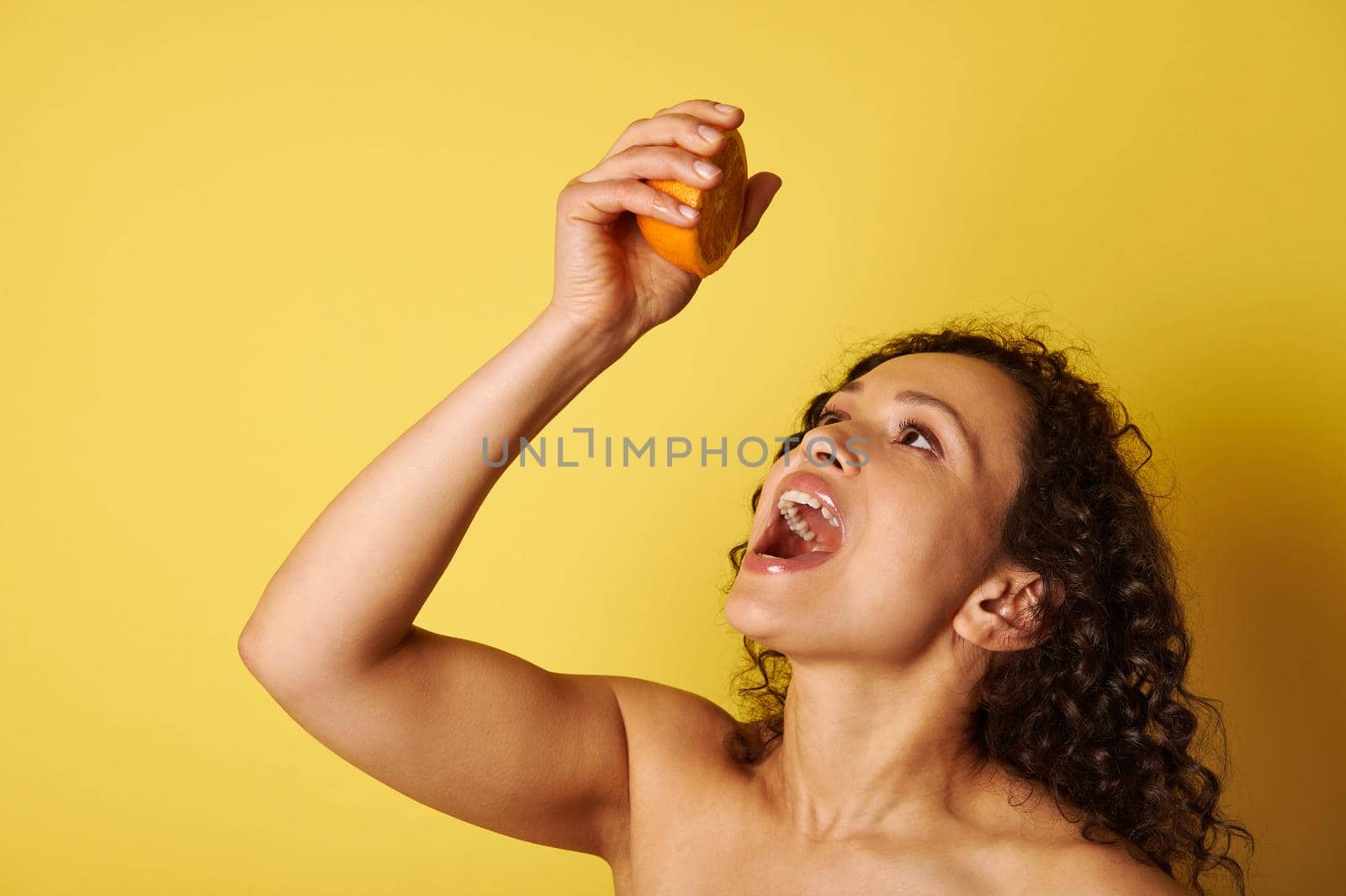 Closeup portrait of a beautiful half naked woman squeezing orange juice into her mouth by artgf