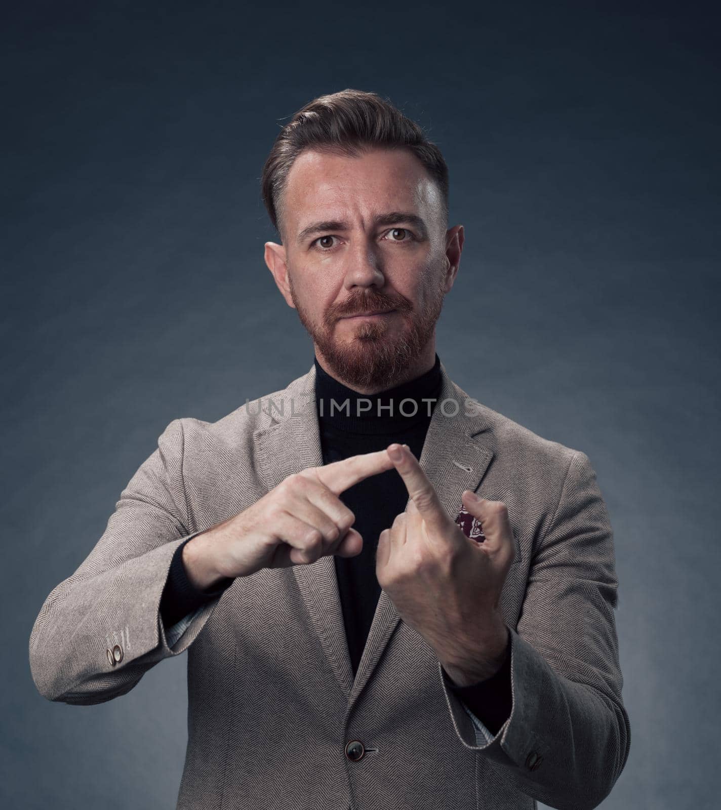 Portrait of a stylish elegant senior businessman with a beard and casual business clothes in photo studio isolated on dark background gesturing with hands. High quality photo