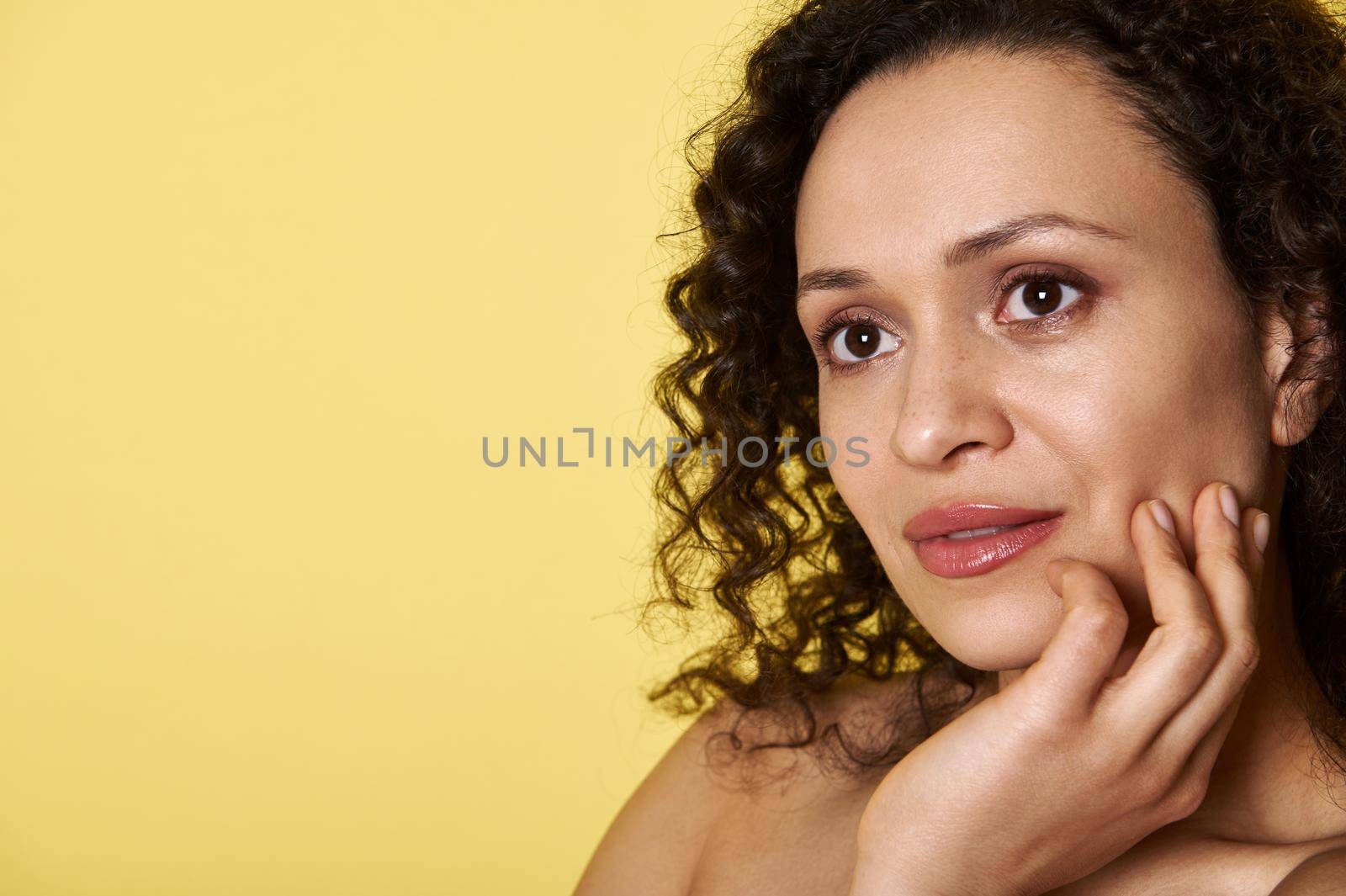 Close Up portrait of a pretty woman with curly hair looking dreamily away isolated on yellow background with copy space