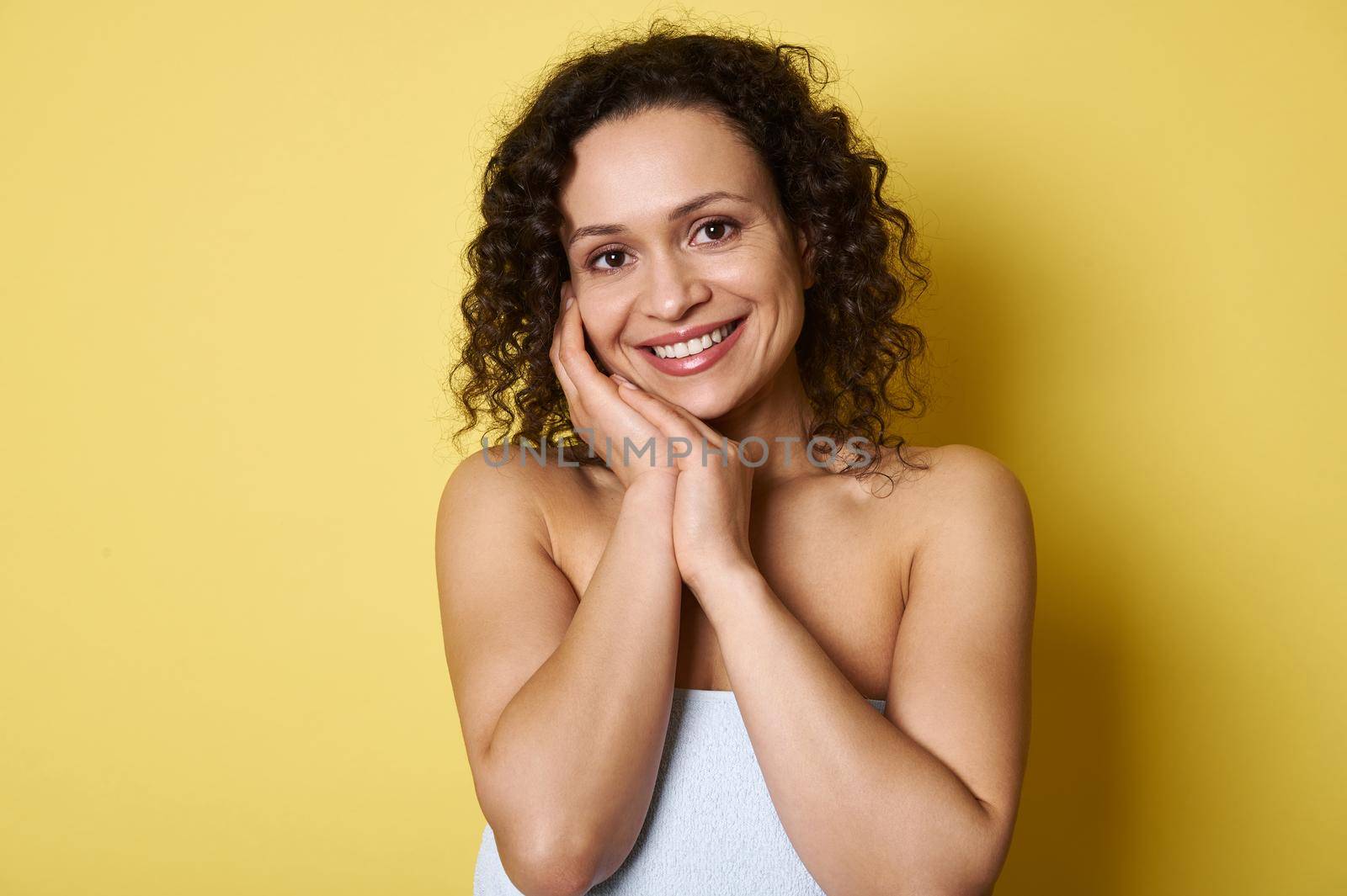 Portrait of beautiful young smiling African American woman with curly short hair, looking at camera while posing over yellow background with copy space